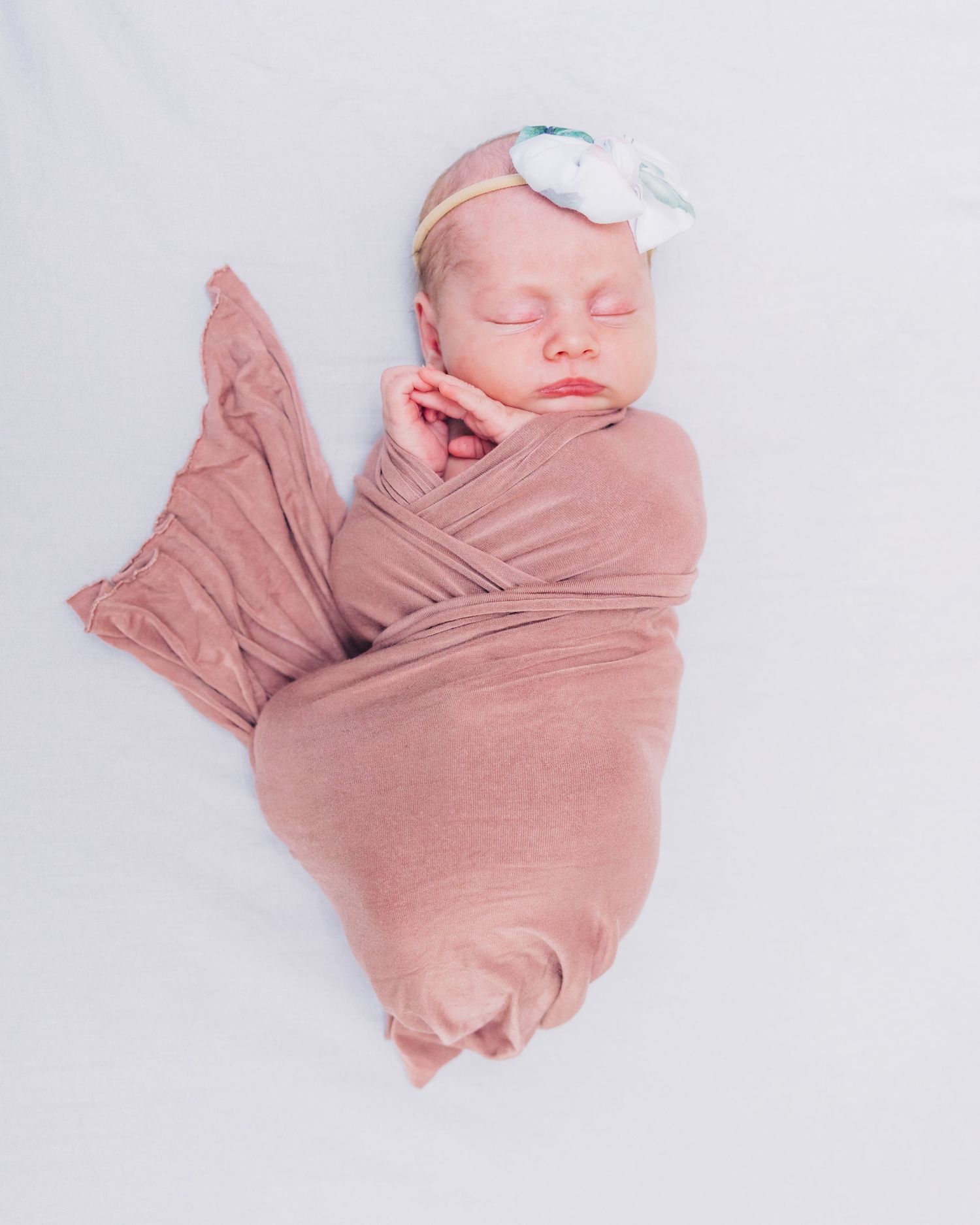 newborn baby in swaddle with her hands poking out near her face