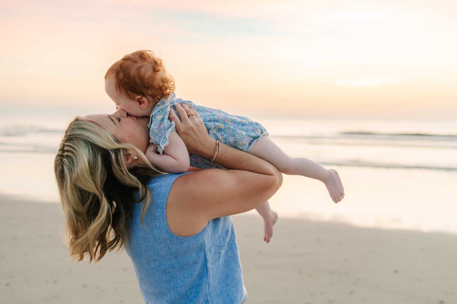 mom holding baby girl over and giving her a big kiss at sunrise in Jacksonville beach, fl