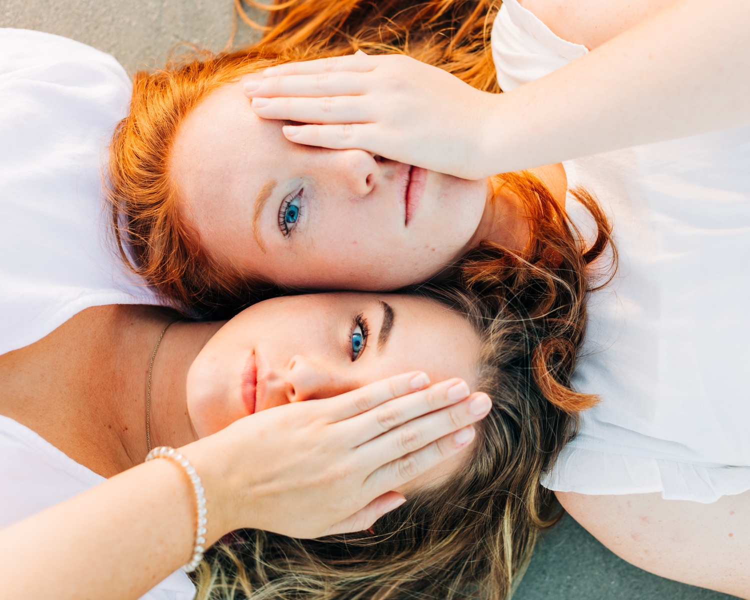two girls on laying on the beach covering an eye