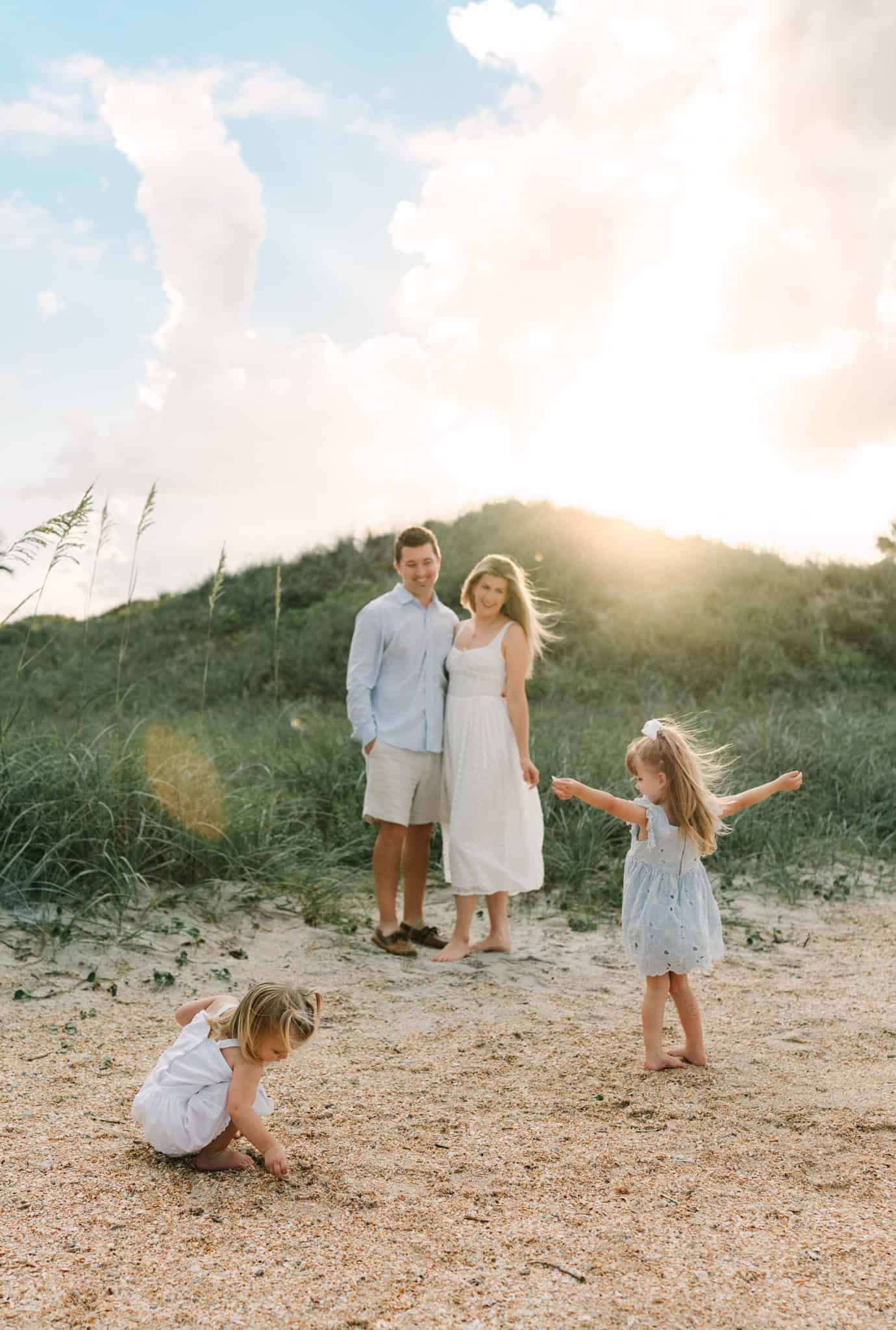 A family of four enjoys a golden hour Ponte vedra beach photoshoot on sandy dunes with sea oats and clouds.