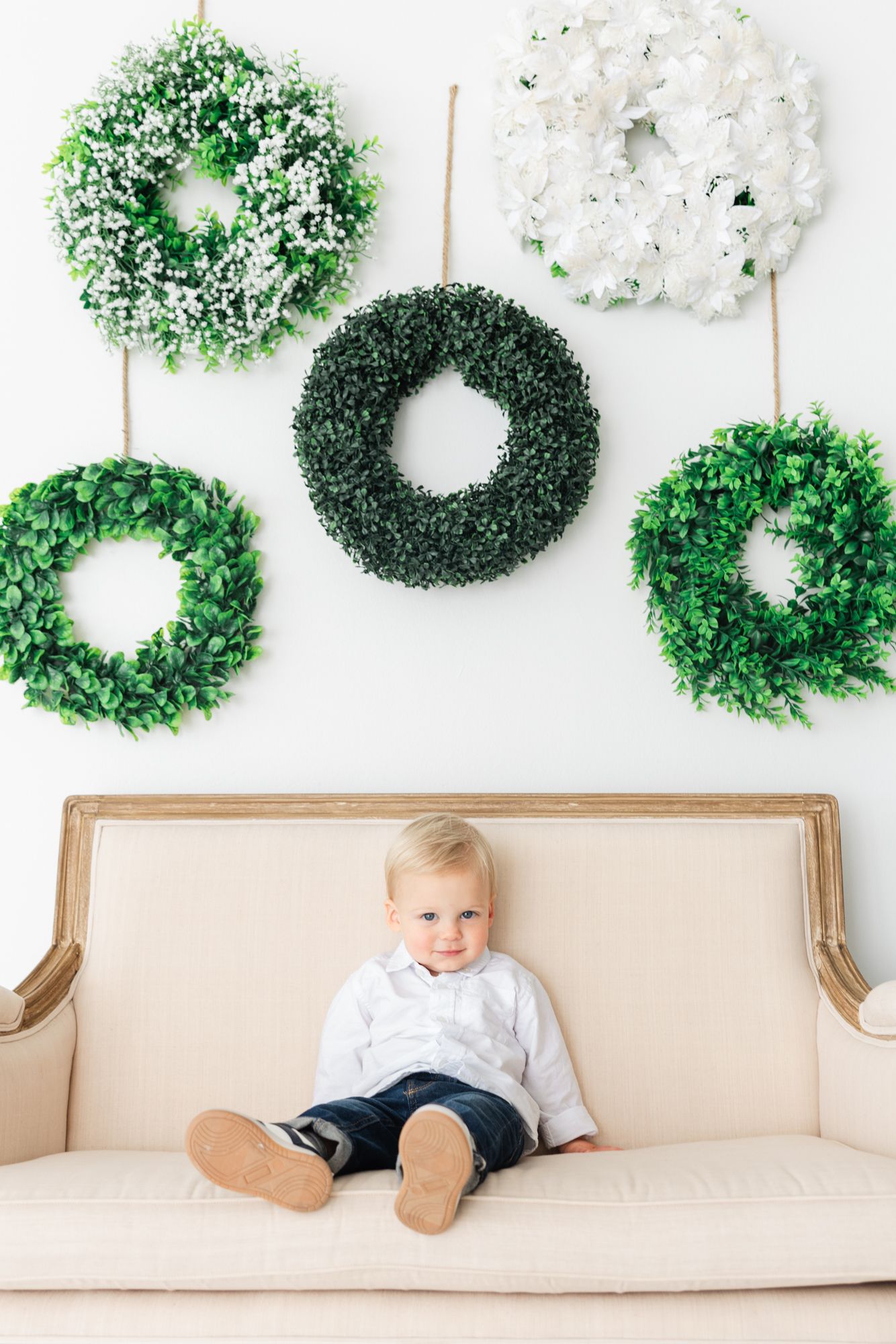 blonde boy sitting on couch with wreaths above him