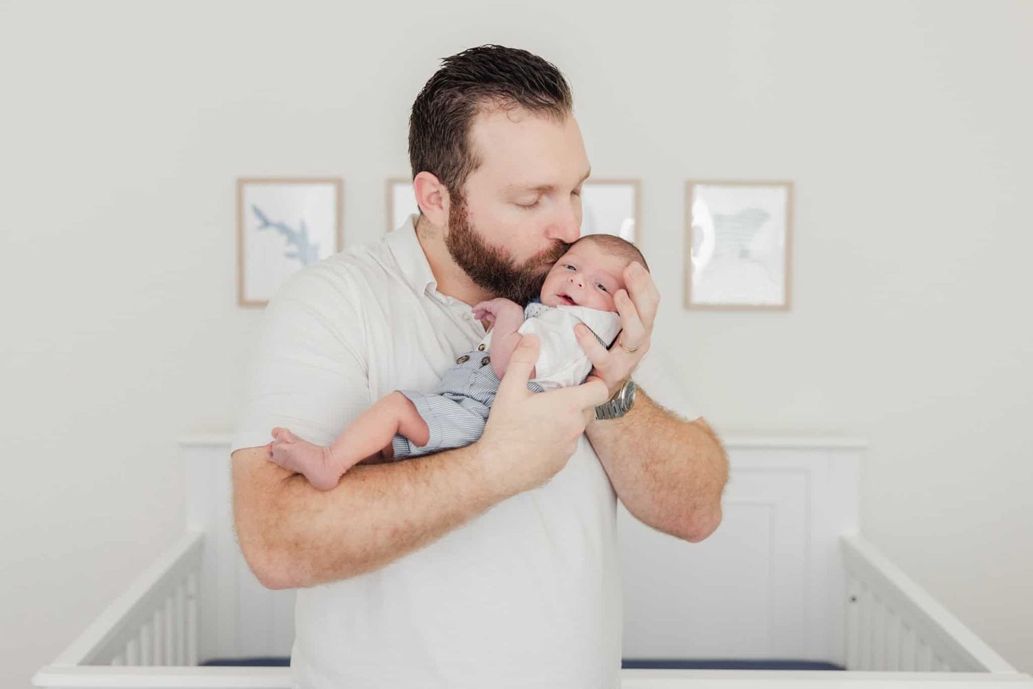dad standing in front of the crib holding newborn boy and giving him a kiss
