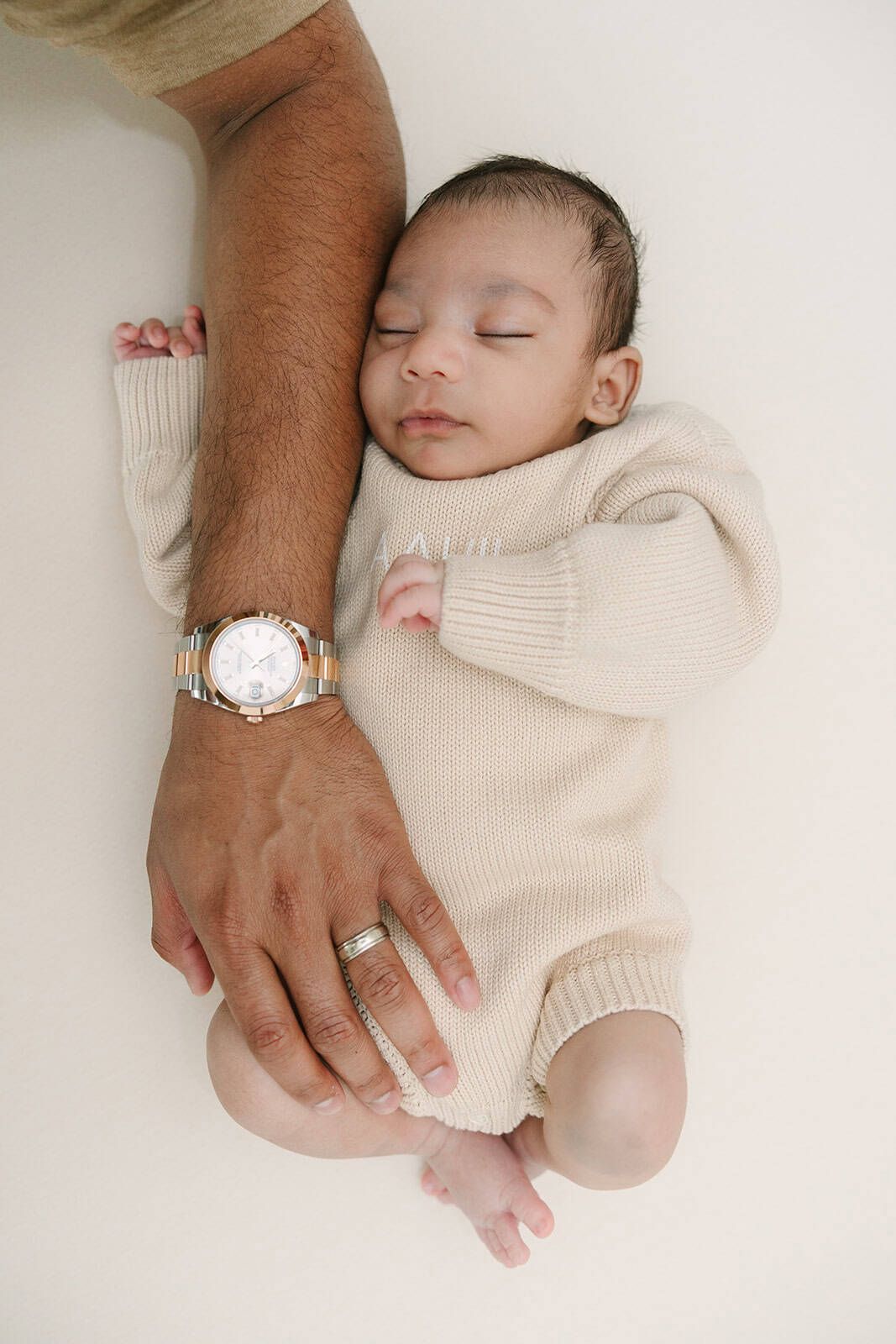 newborn baby boy in a sweater with dads hand coming down from above and baby is holding his arm
