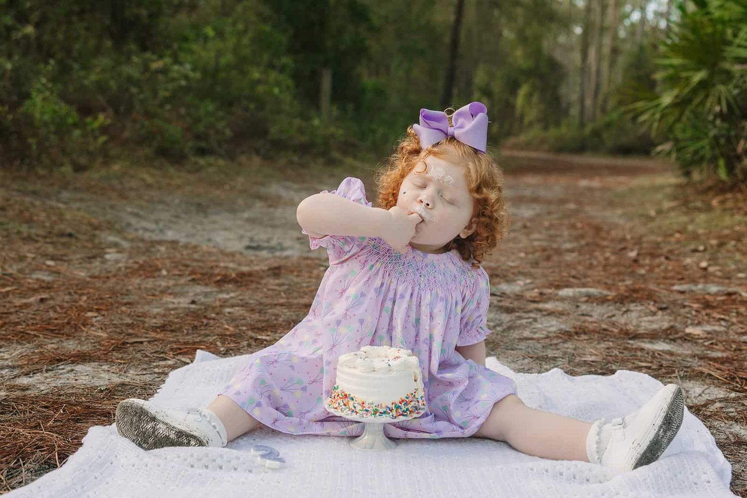 toddler girl eating birthday cake, licking her fingers because its so yummy
