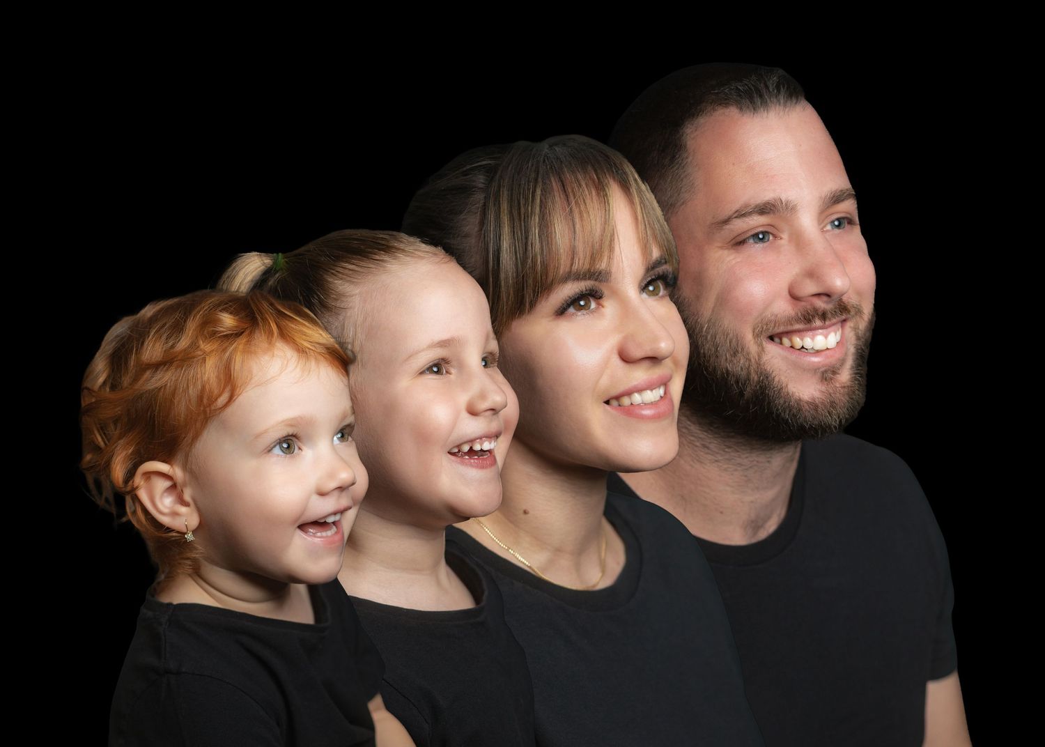 A family of four poses together in profile against a dark background, smiling warmly in matching black attire.