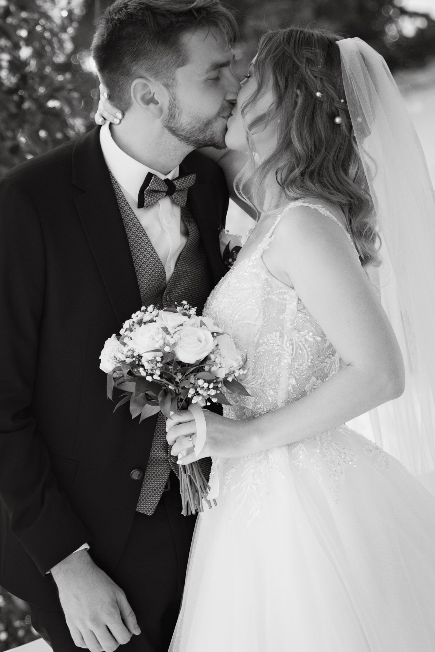 Black and white wedding photo of a bride and groom sharing a kiss, bride holding a floral bouquet.