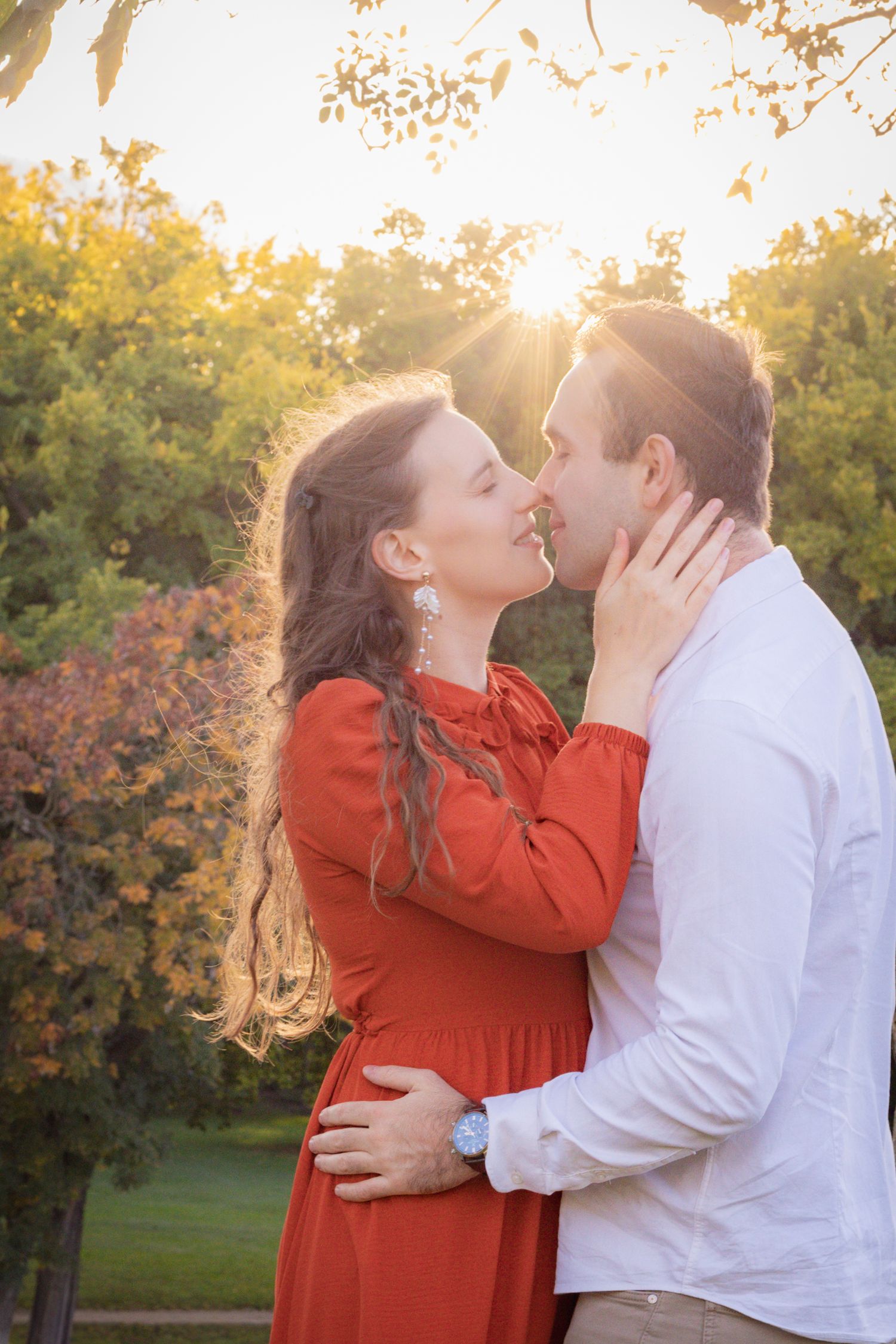 A romantic sunset moment captured between a couple wearing red and white in a park setting.