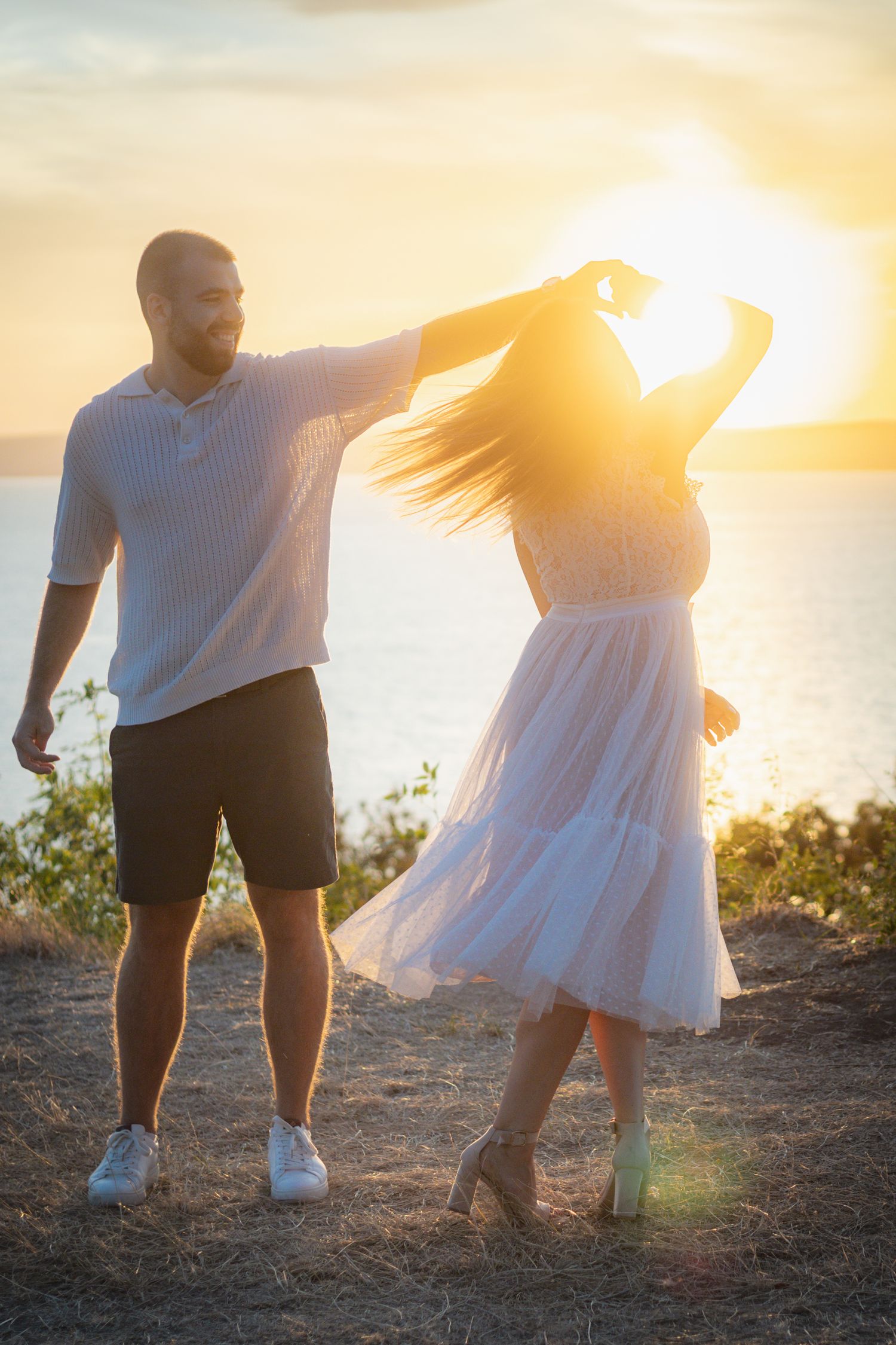 A couple dances together on a cliff overlooking the ocean at sunset.