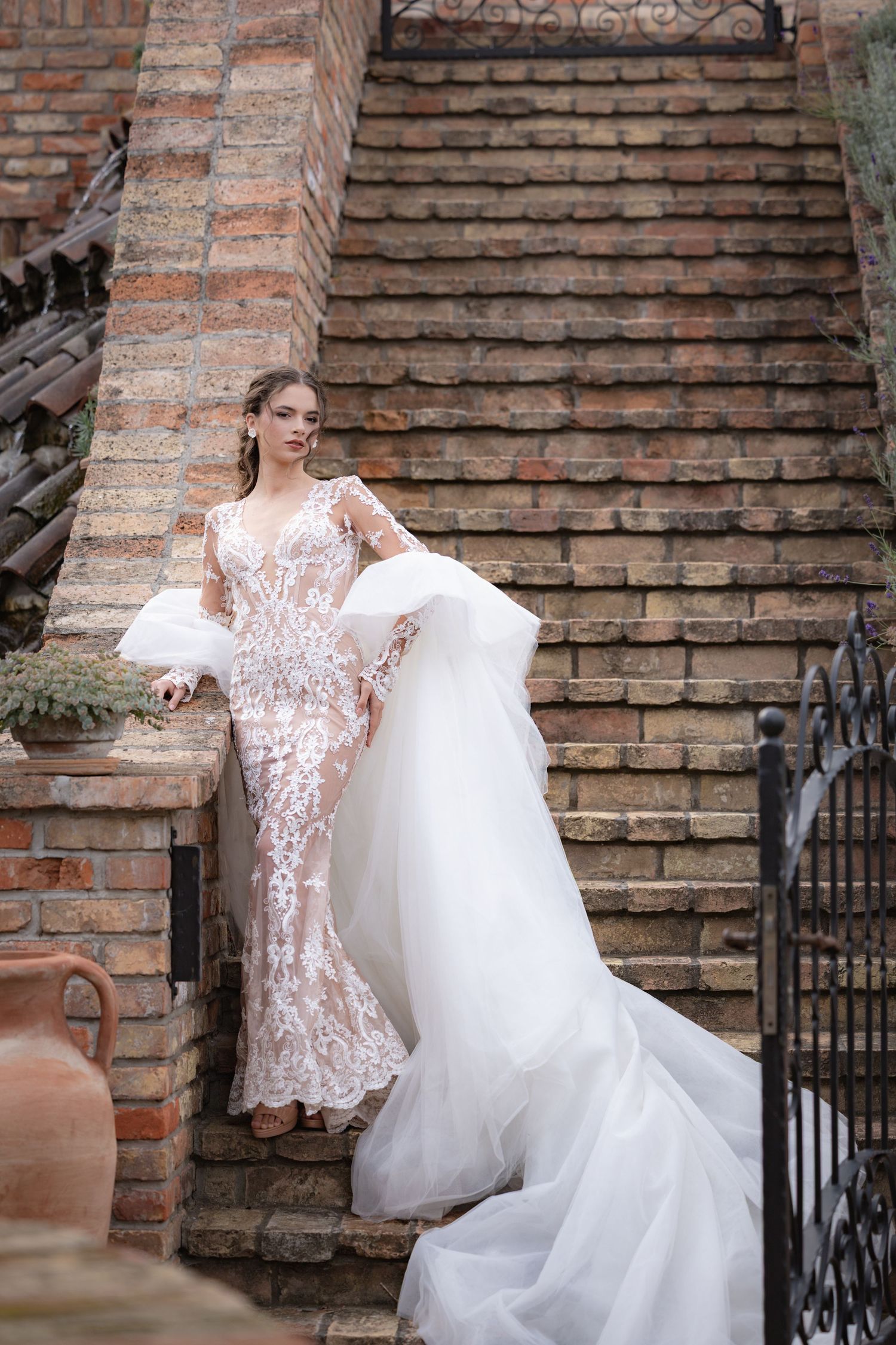 A bride's white lace wedding dress flows elegantly on brick steps.