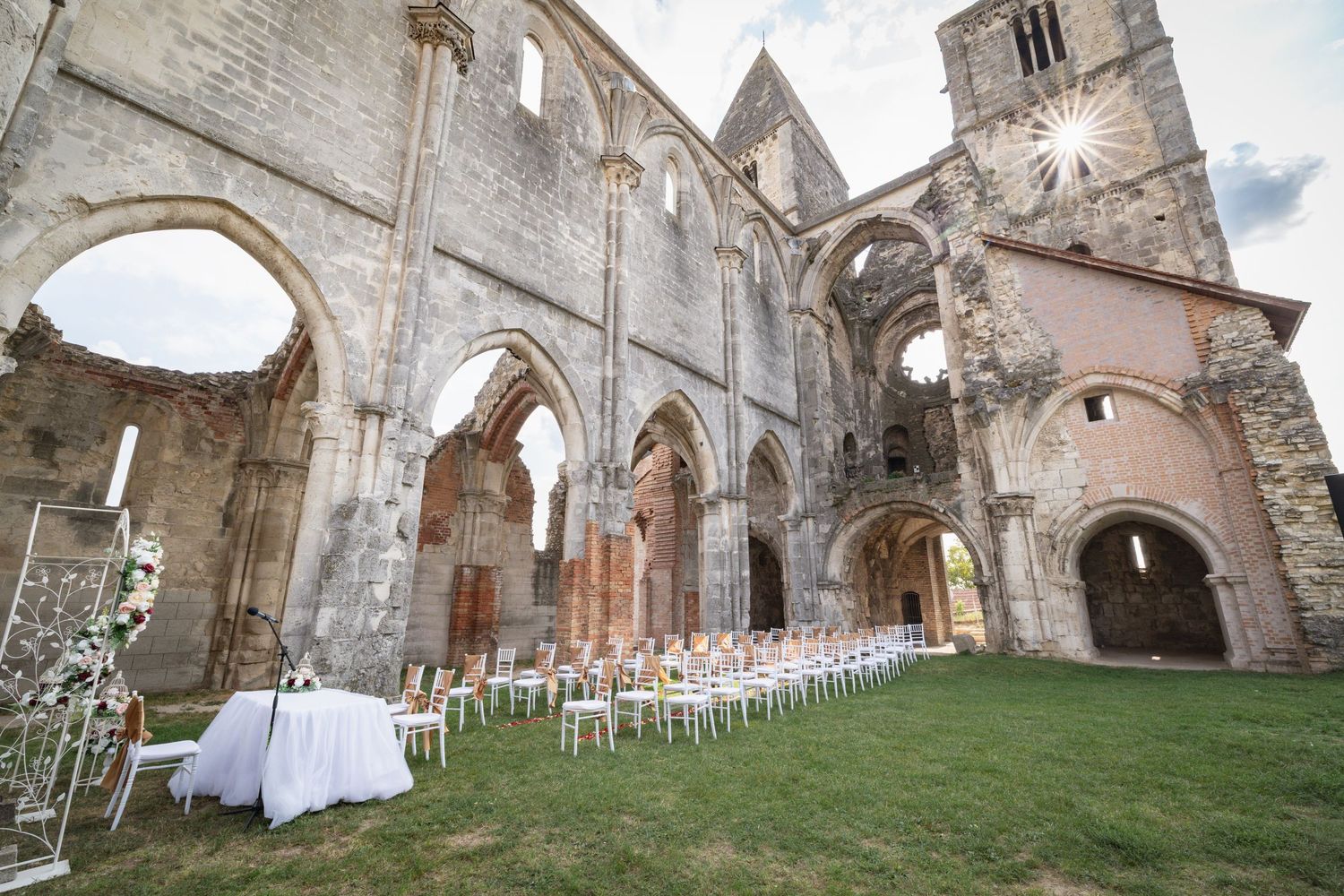 Gothic stone church ruins with arched windows and doorways set up for an outdoor wedding ceremony with white chairs.