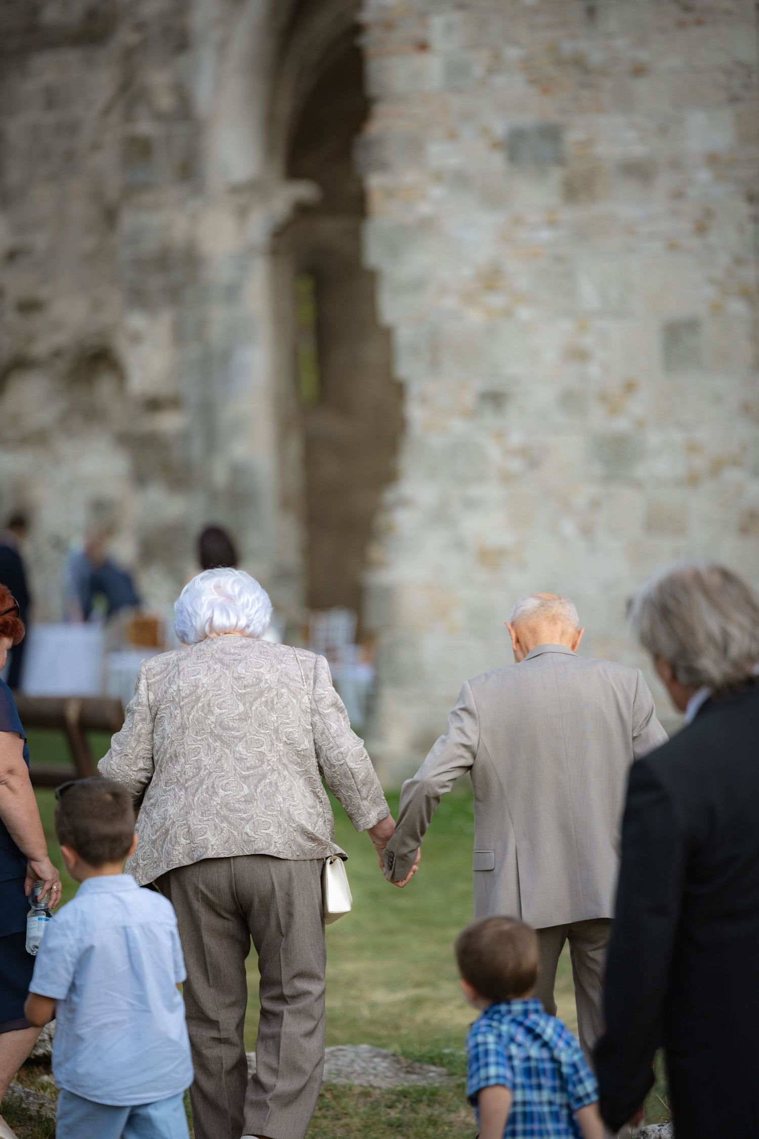 Wedding guests gather outdoors near stone walls during a celebration.
