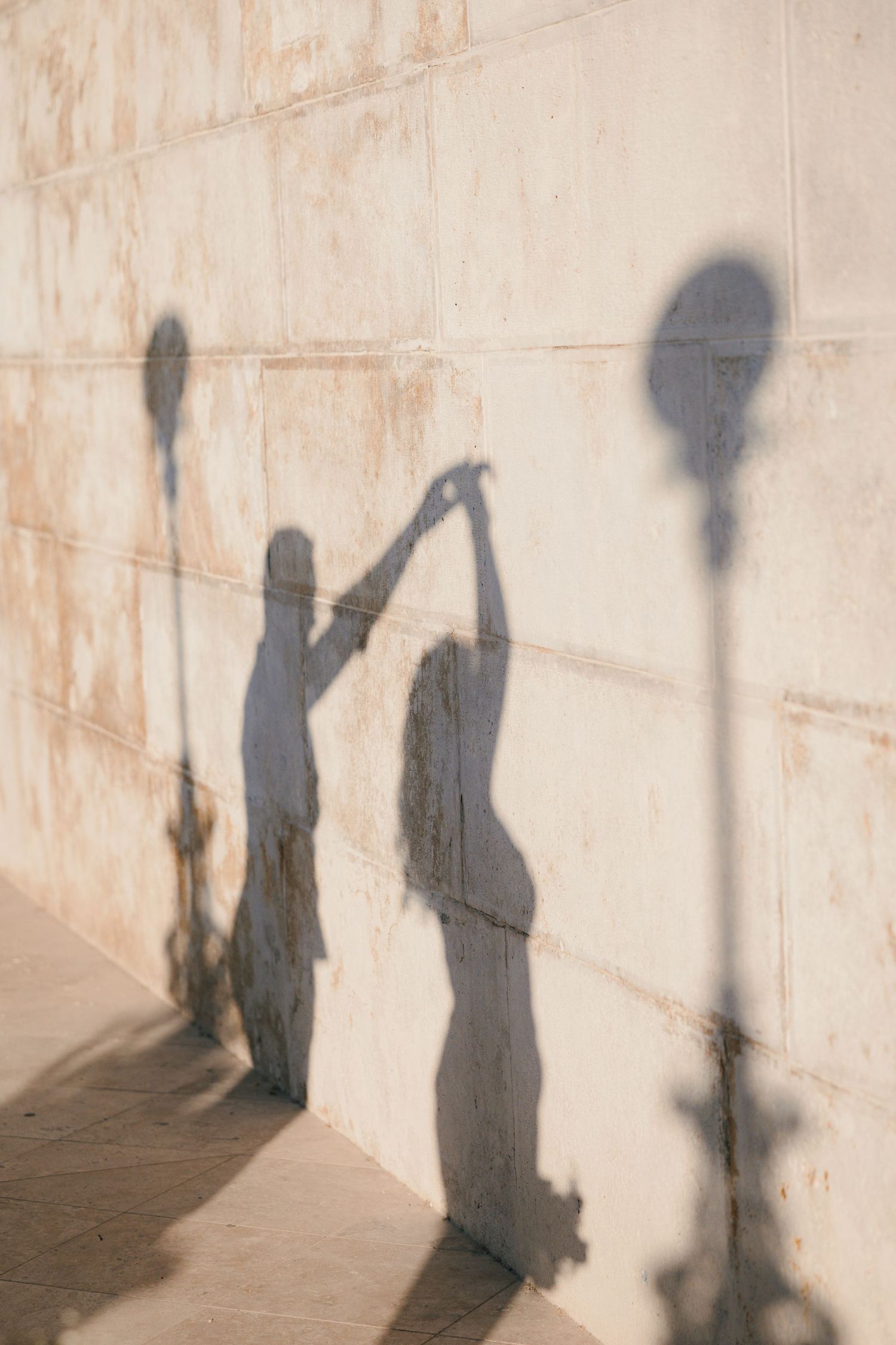 Shadows of two people dancing cast on a sunlit stone wall with lamp post silhouettes.