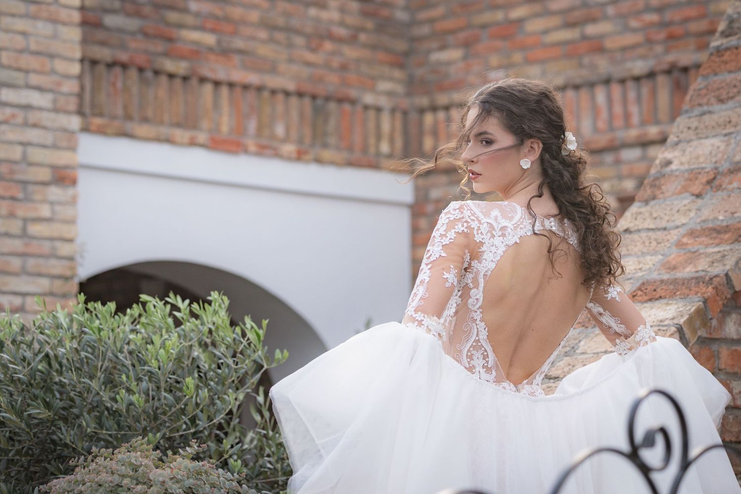 Delicate lace details and flowing fabric of a wedding dress in a rustic brick setting.