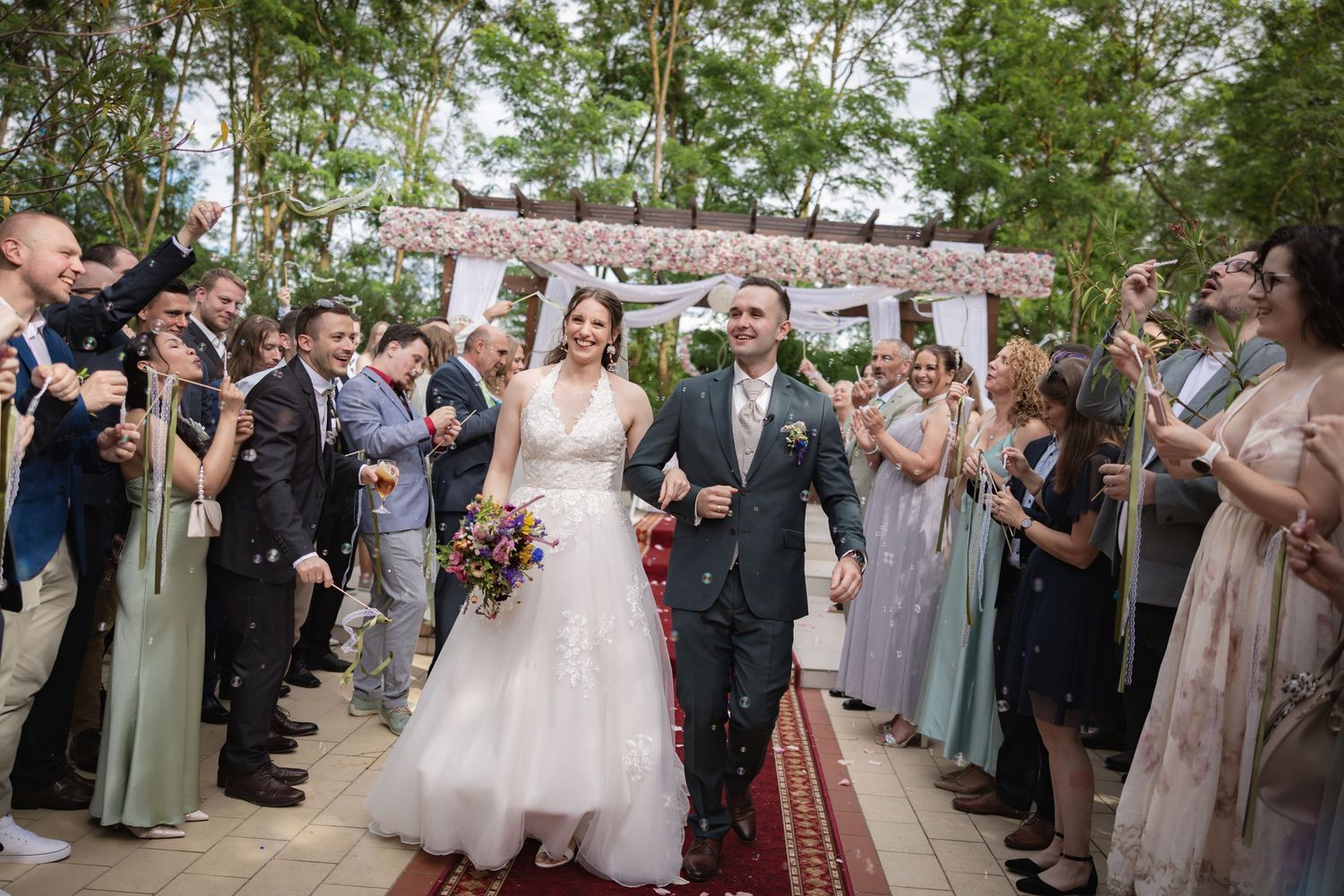 Bride and groom walk down the aisle as guests celebrate with confetti at an outdoor wedding ceremony.