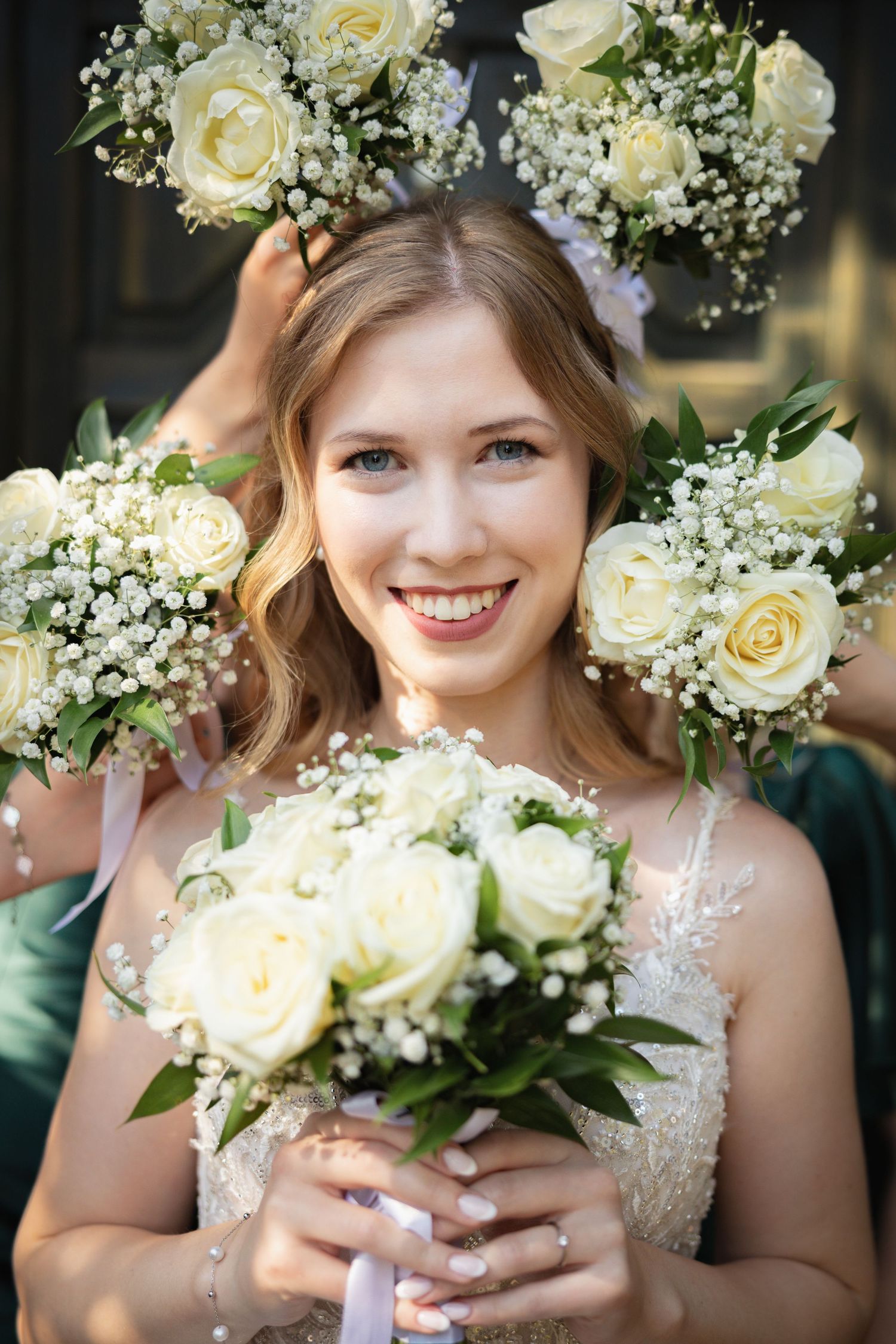 Smiling bride holding white rose bouquet, surrounded by bridesmaids with matching floral arrangements and flower crowns.