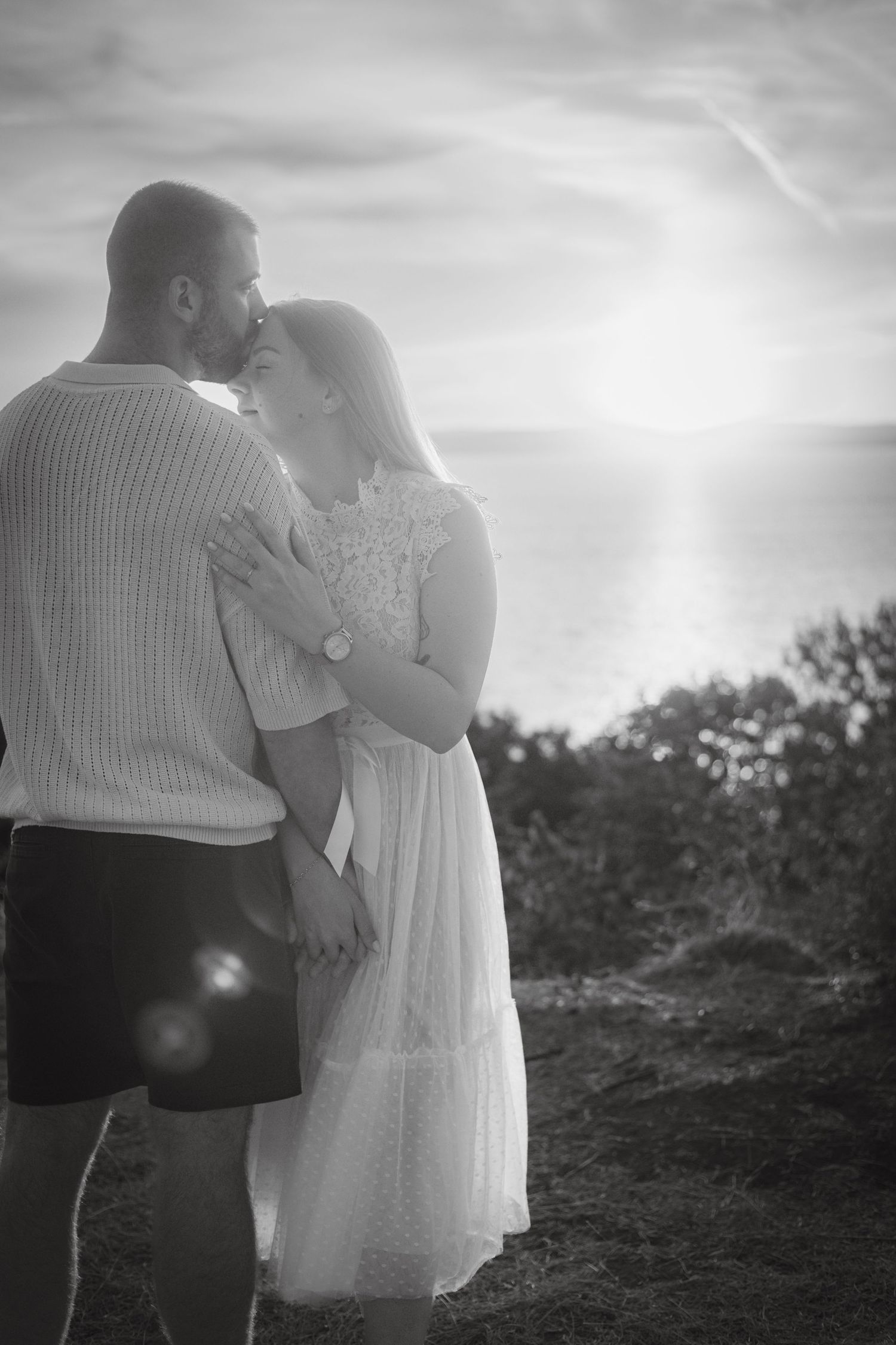 A black and white silhouette of a couple embracing against a bright sky.