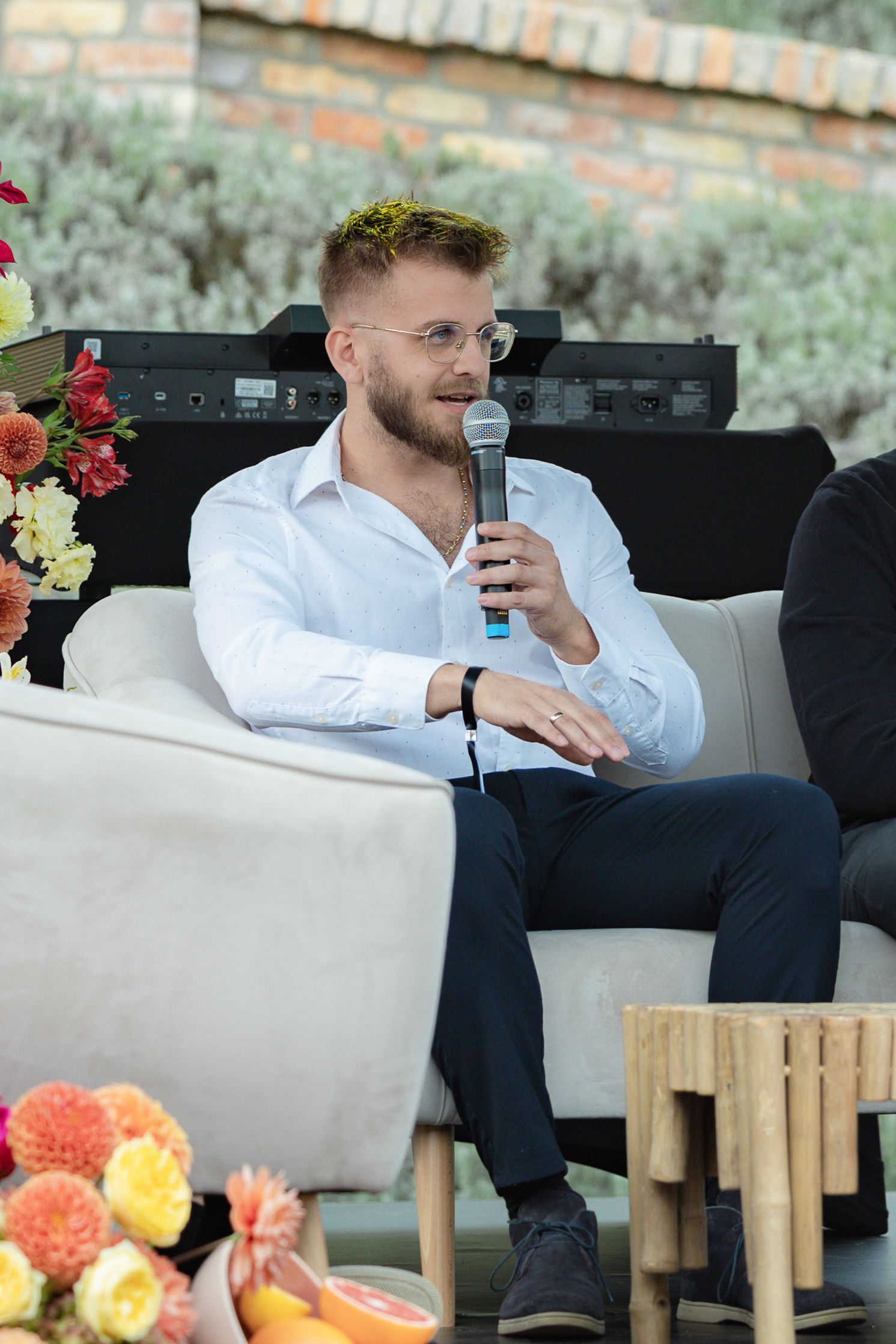 A person in a white shirt relaxes on an outdoor patio couch with colorful flowers in the background.