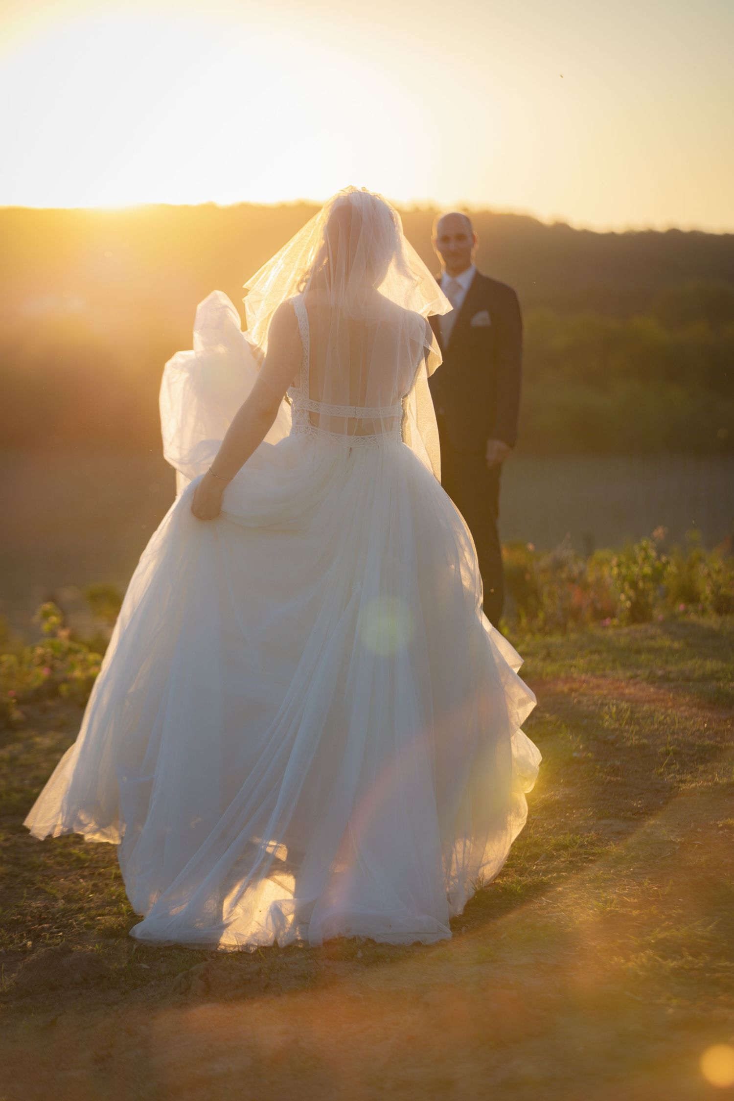 Ethereal sunset wedding photo with flowing white dress silhouetted against golden light.