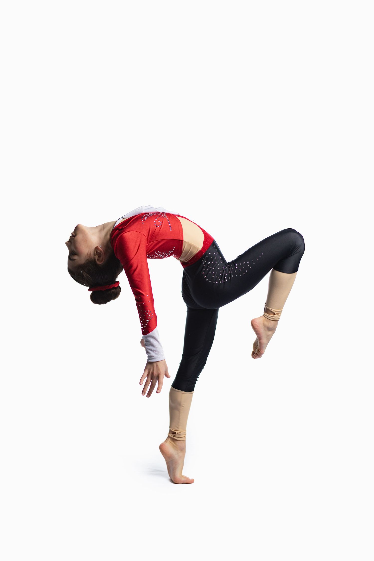 Young female gymnast in red and black leotard performing a backbend balance pose on one leg against white background.