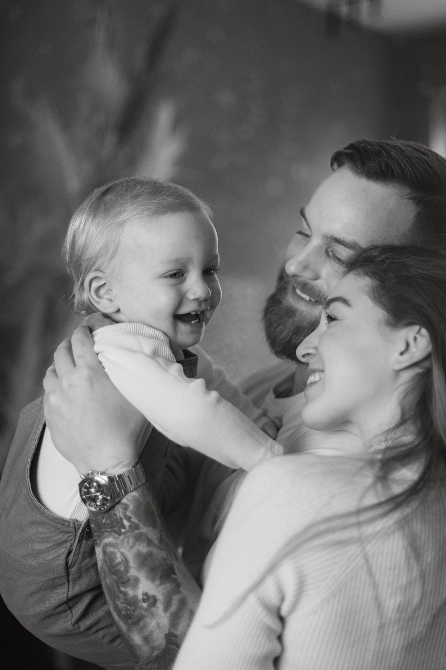 Black and white photo of happy parents holding their laughing baby, sharing a joyful family moment together.