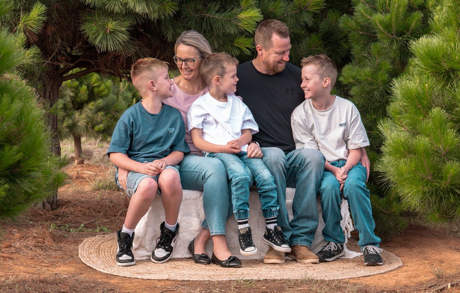 Row of people sitting casually on wooden steps with evergreen trees behind them.