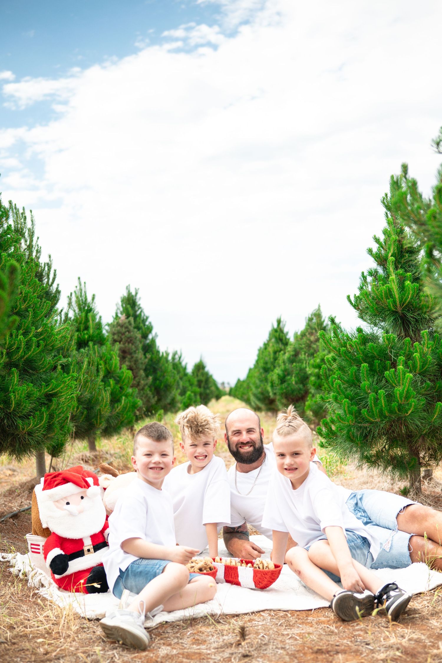 Family group photo on a blanket surrounded by pine trees on a sunny day.