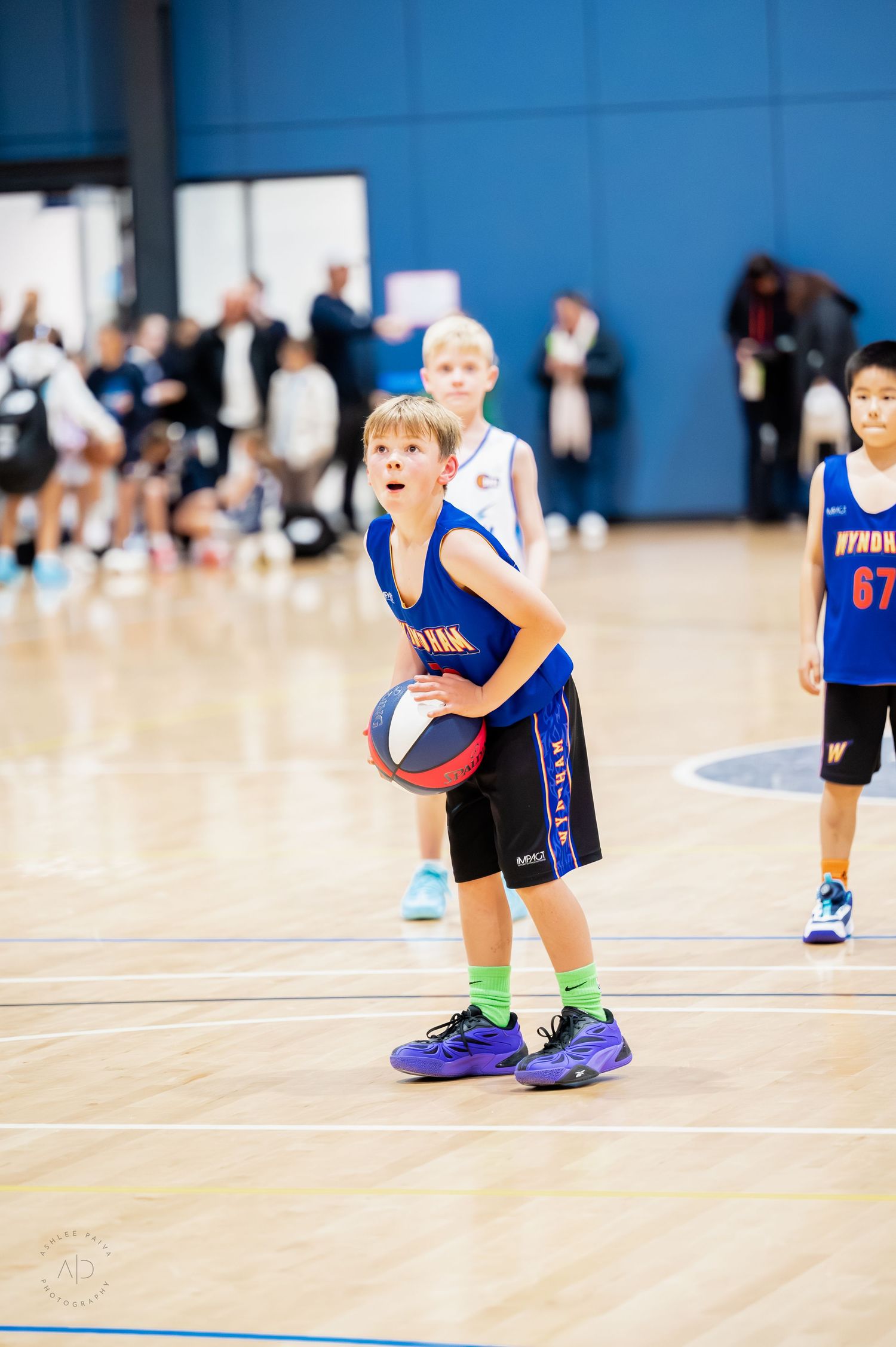 Young boy in blue basketball uniform dribbling on indoor court during youth basketball game.