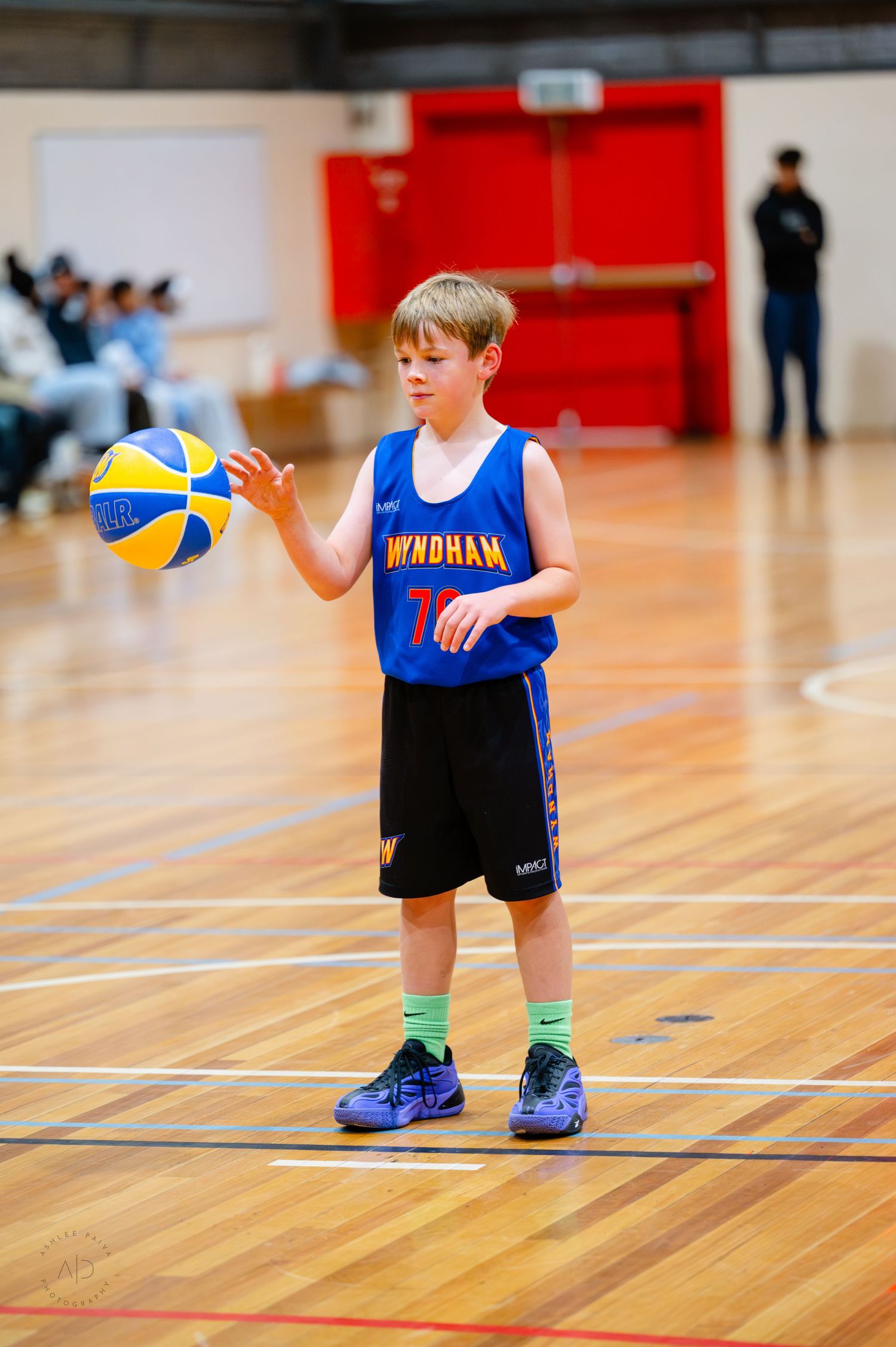 Young boy in Wyndham basketball uniform holding a ball on an indoor court during a youth basketball game.