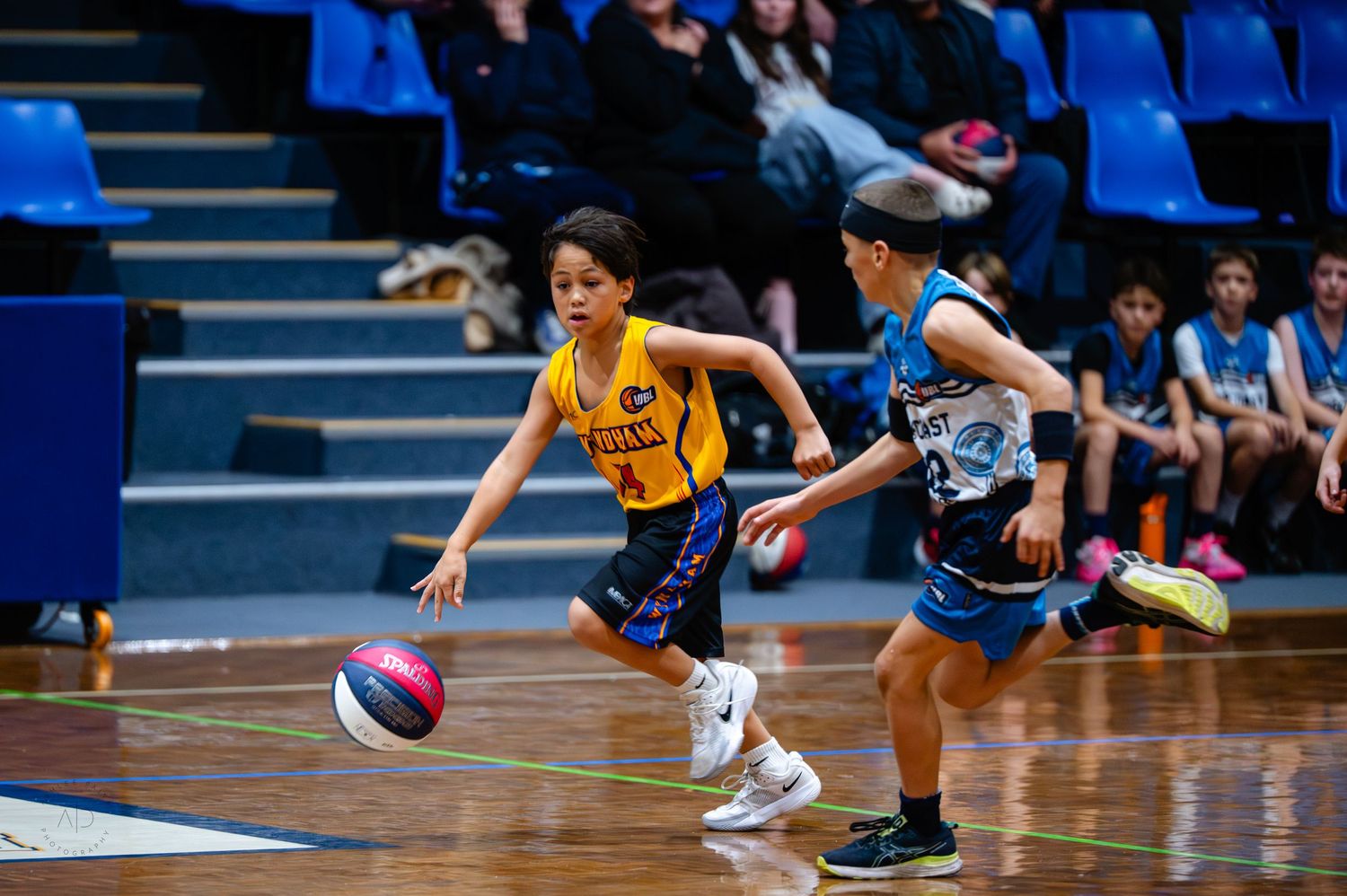 Young boy in yellow jersey dribbles basketball during indoor youth basketball game.