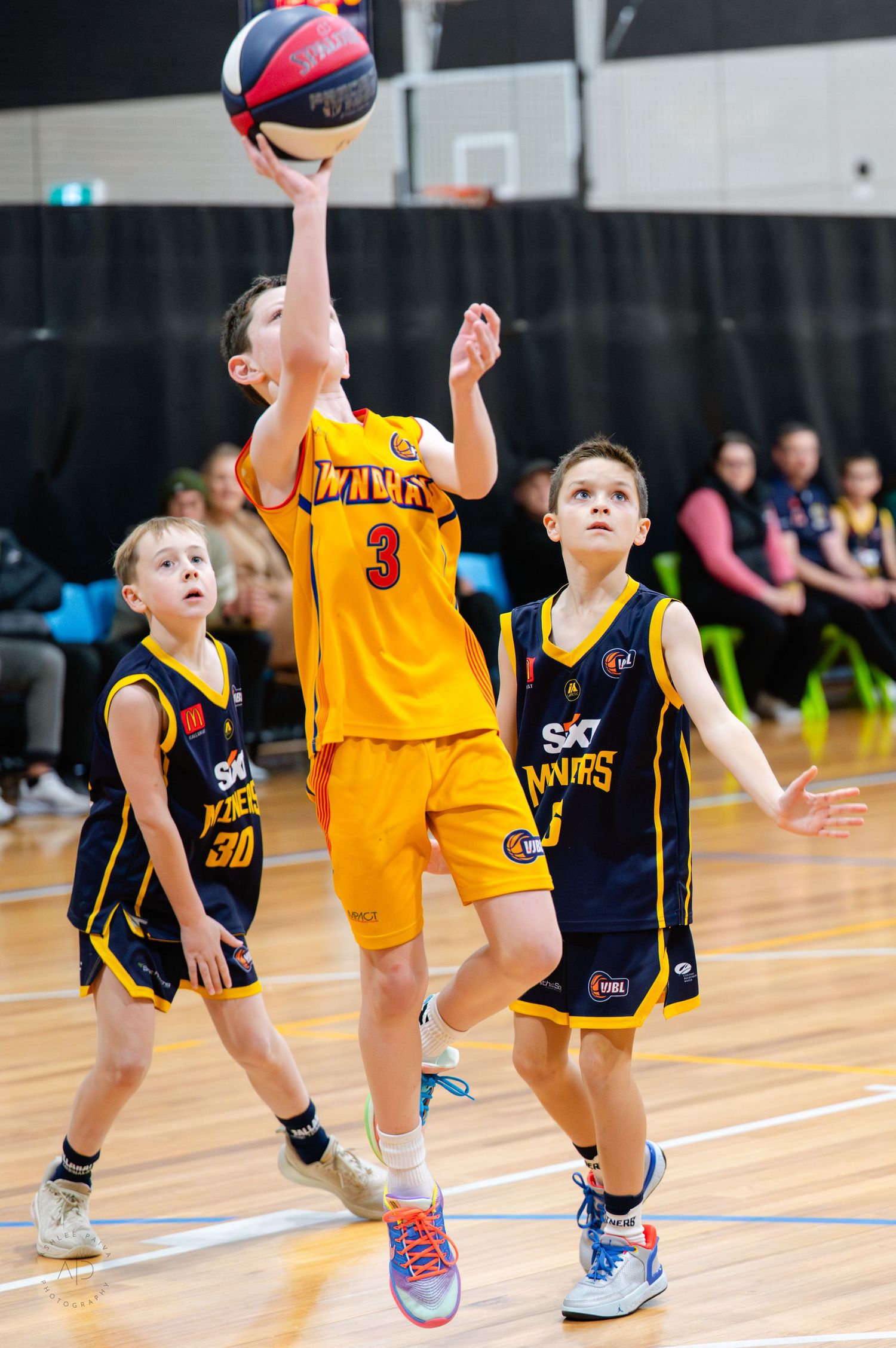 Young basketball player in yellow jersey #3 attempts a layup during a youth basketball game.