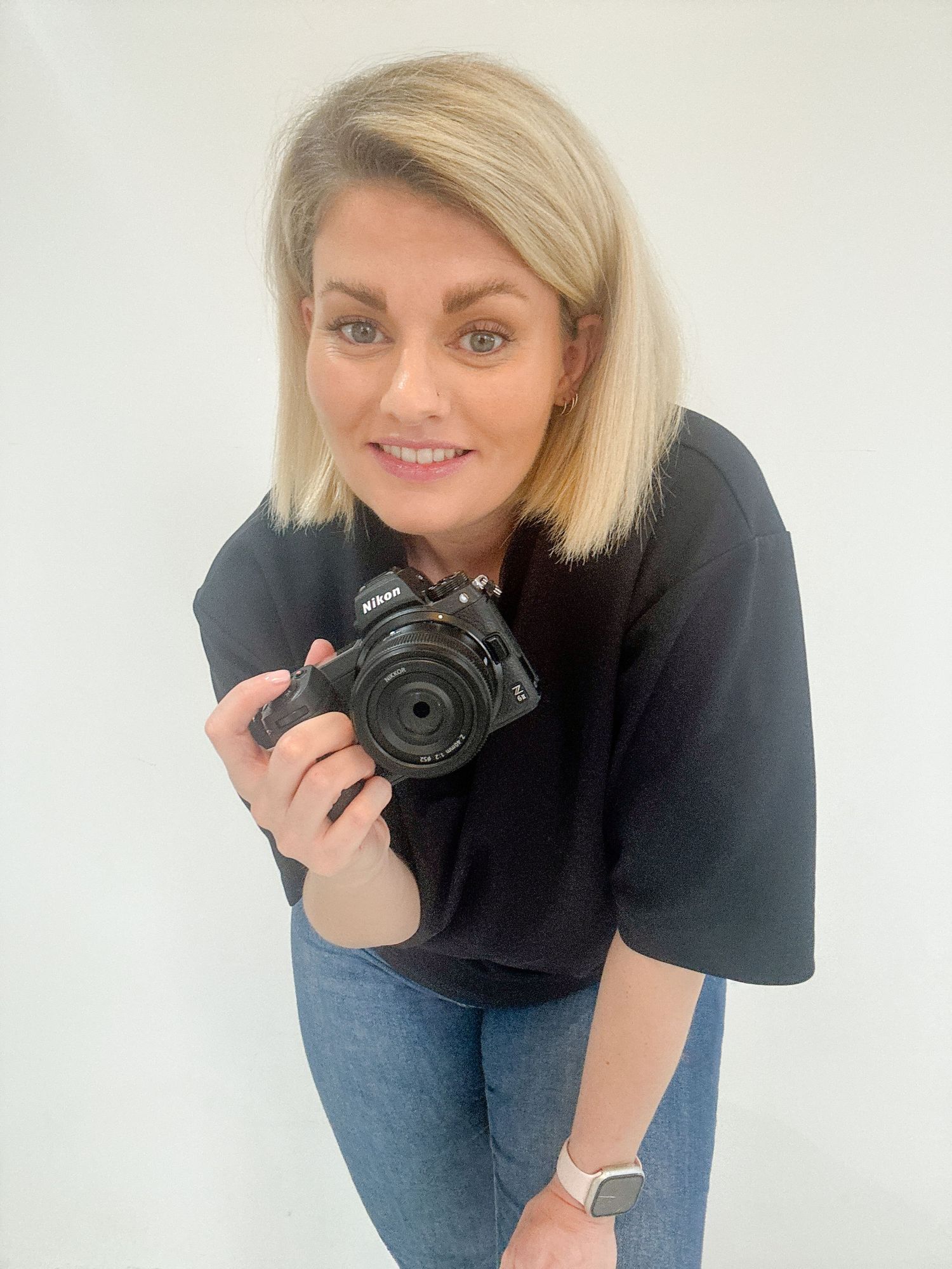 Photographer holding DSLR camera while wearing black top against white background.