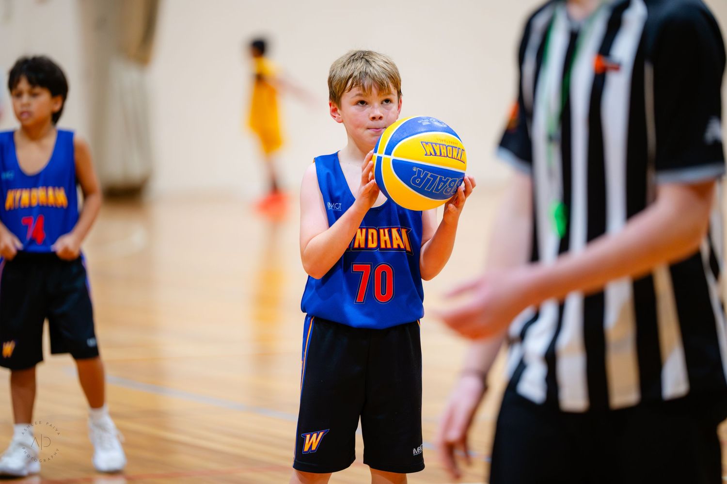 Young boy wearing number 70 basketball jersey holding ball during youth basketball game indoors.