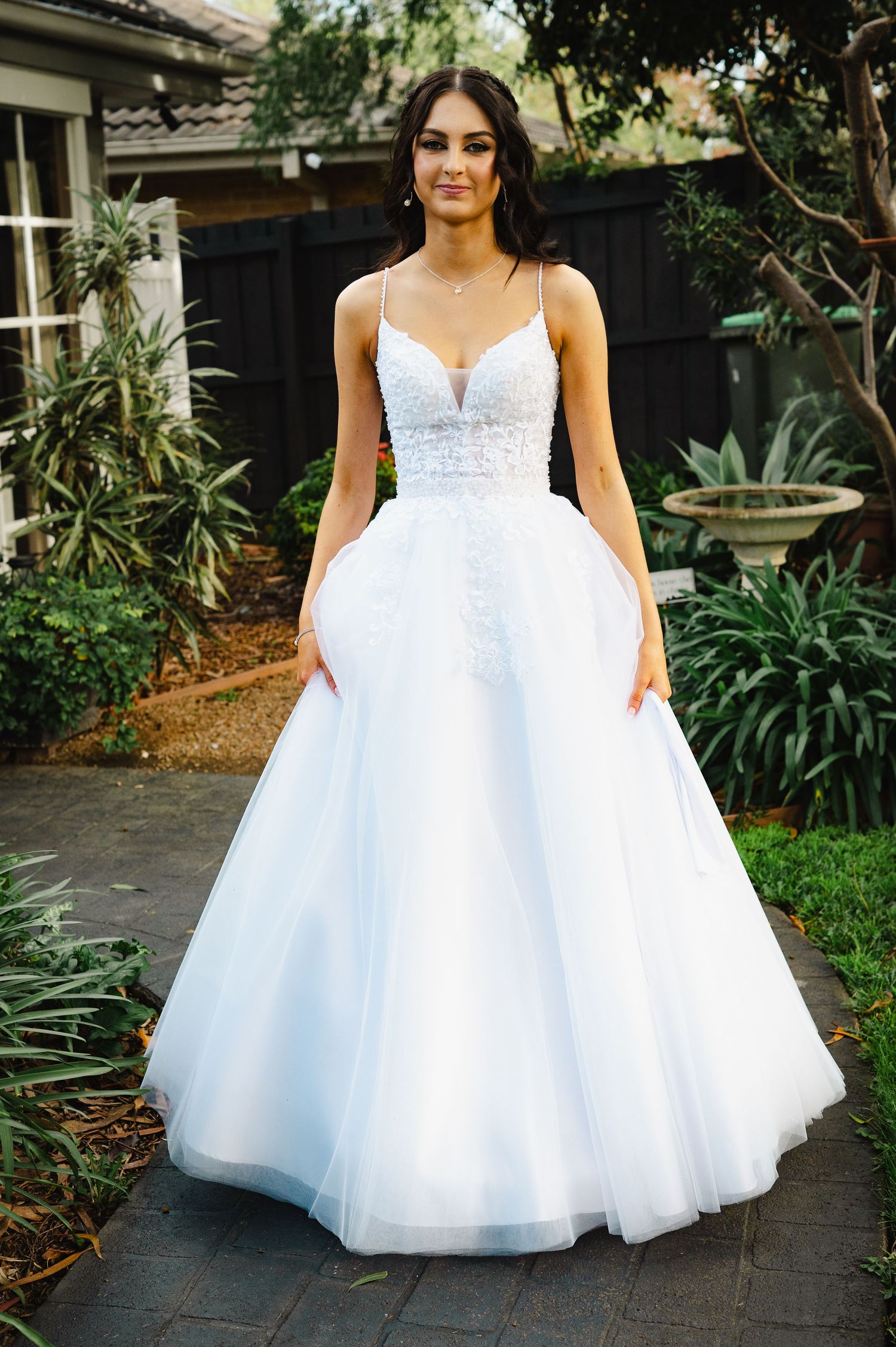 Elegant white bridal ball gown with lace bodice, spaghetti straps, and flowing tulle skirt worn outdoors.