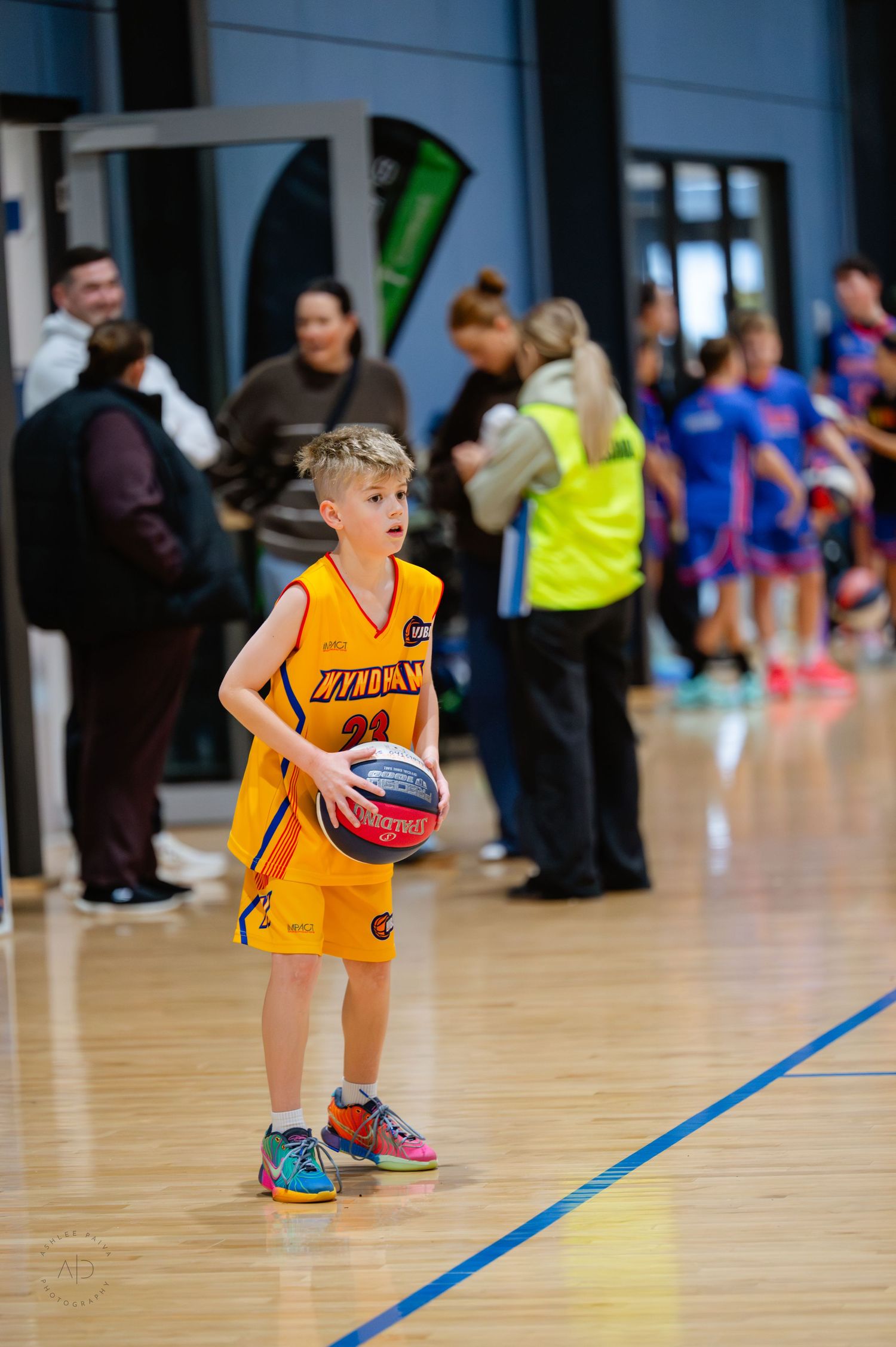 Young boy in yellow basketball uniform #21 holds ball on indoor court during youth basketball game.