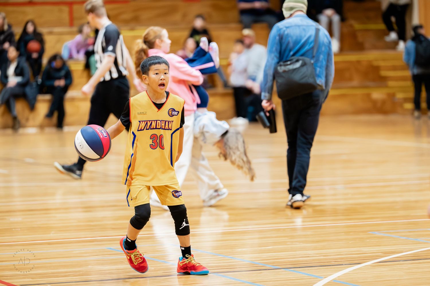 Young basketball player dribbling ball during indoor youth game, wearing yellow Franklin jersey number 34.
