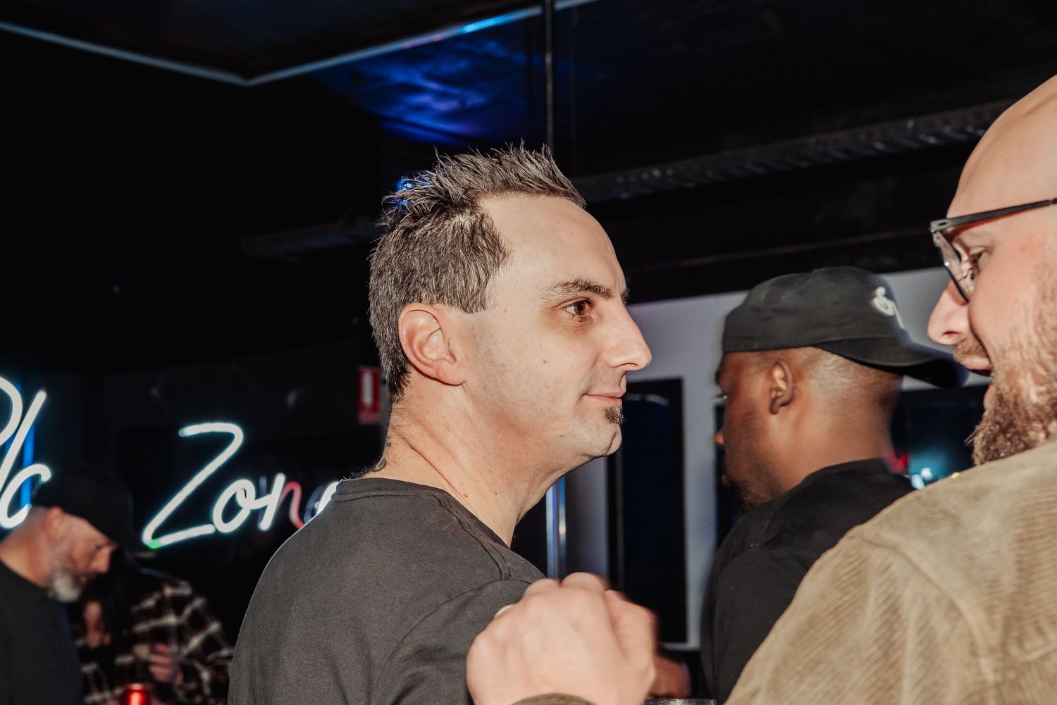 Men socializing at a nightclub event with neon signs glowing in the background.