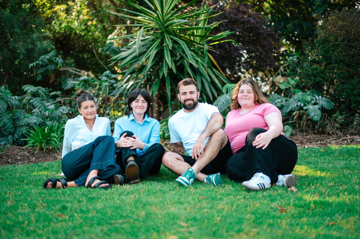Group relaxing on green grass during an outdoor photo session with trees in background.