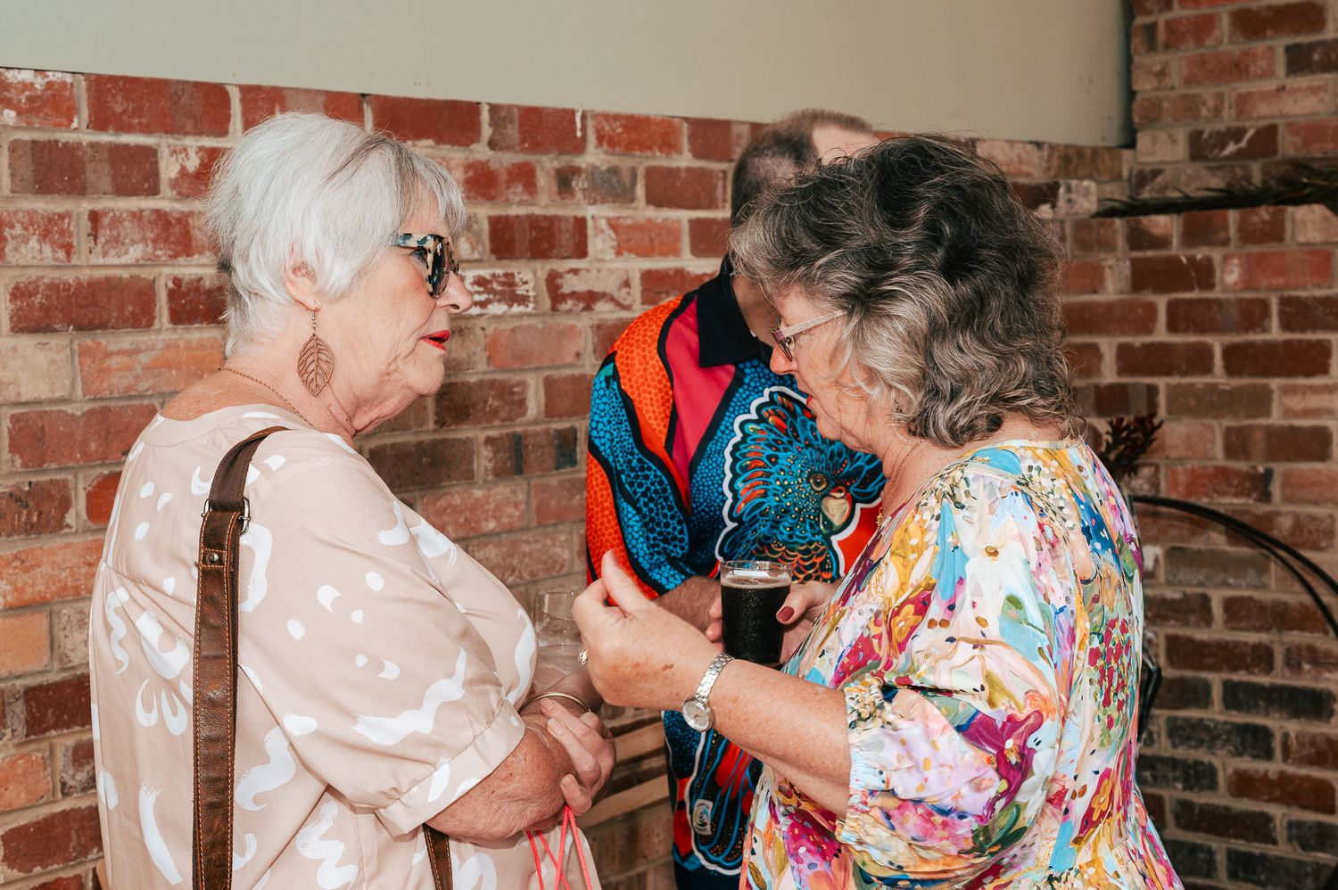 Group of elderly people in colorful outfits dancing together at a social gathering with brick walls in the background.