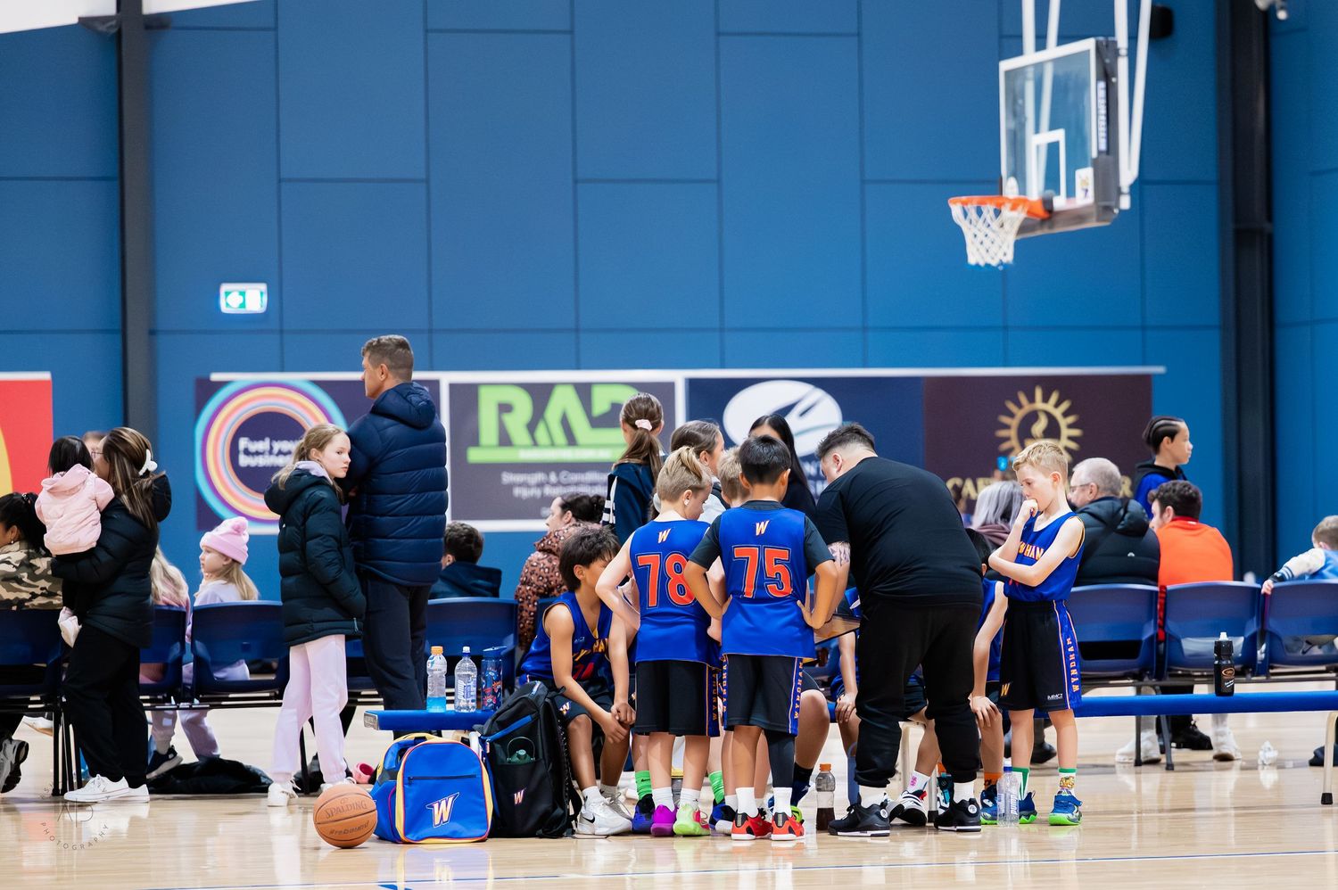 Young basketball players huddle with coaches during a youth tournament game inside a modern indoor sports facility.