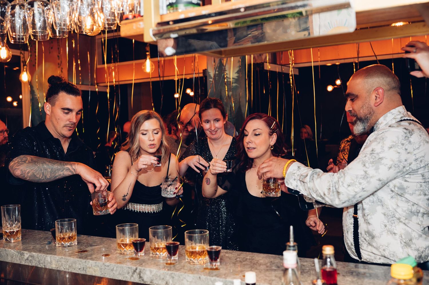 Group of friends sharing drinks and laughter at a bar counter during a celebration.