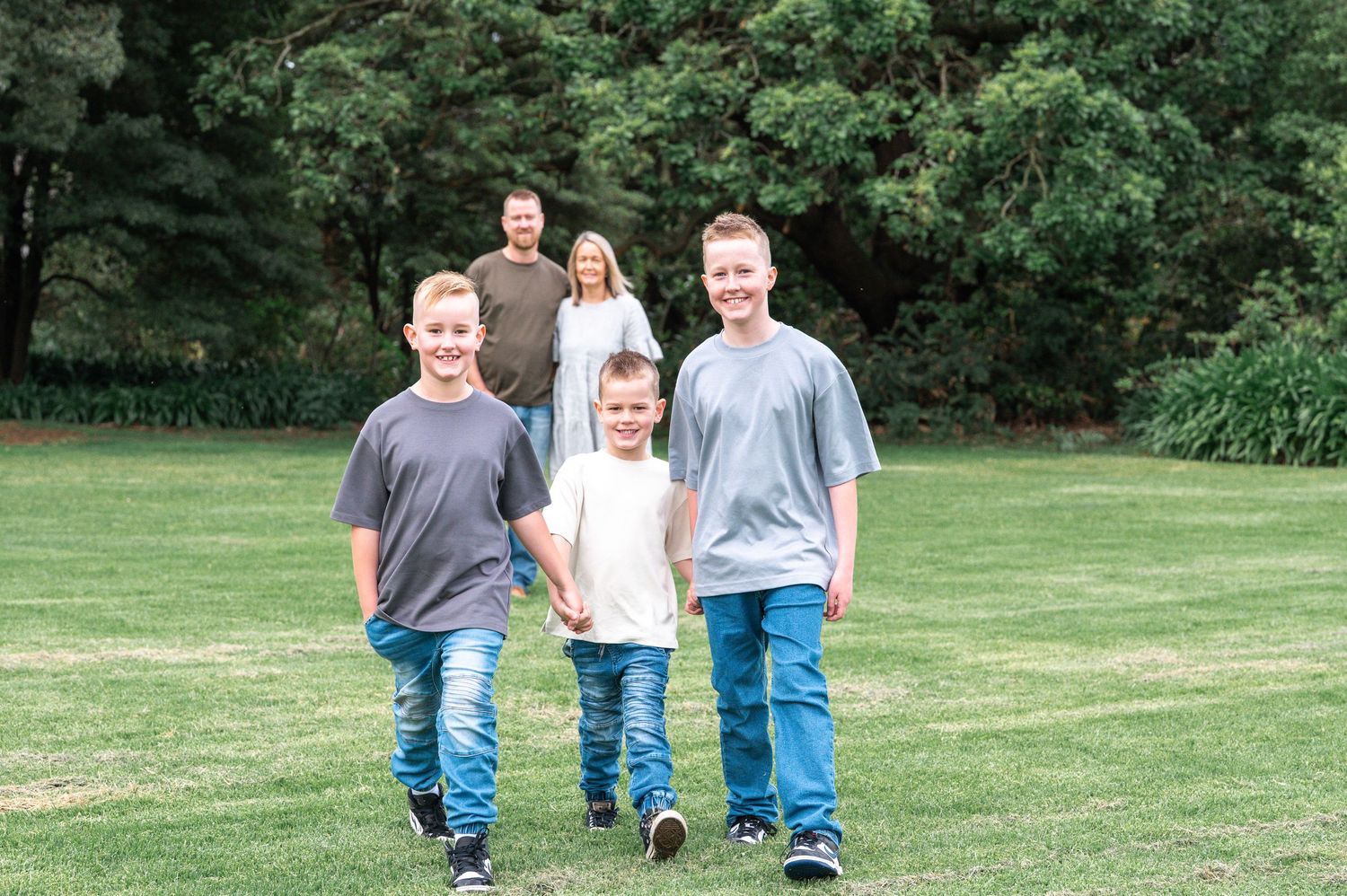 Outdoor family photoshoot in a grassy field with natural greenery backdrop.