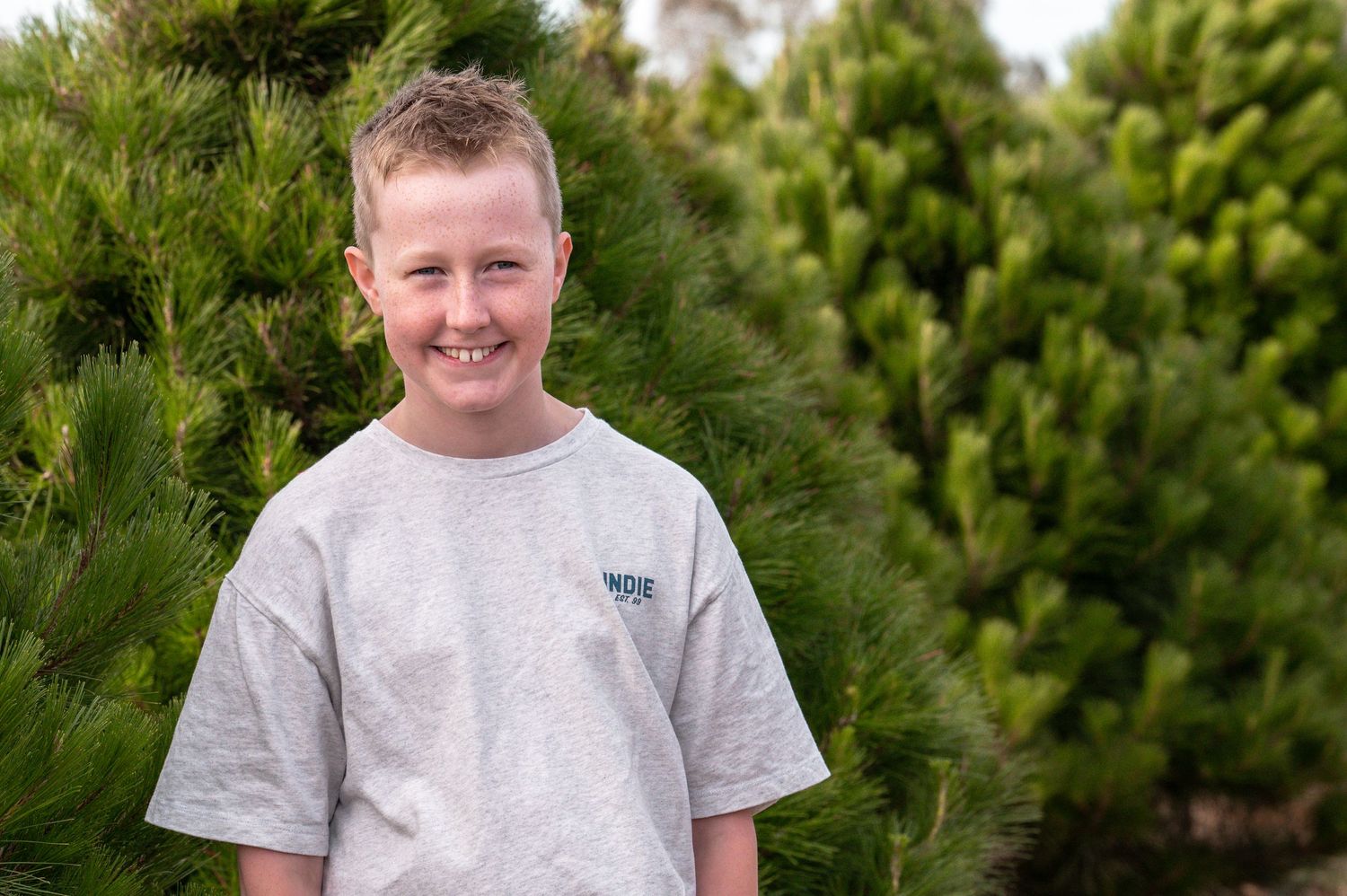 Casual portrait against vibrant green pine tree background in natural lighting.