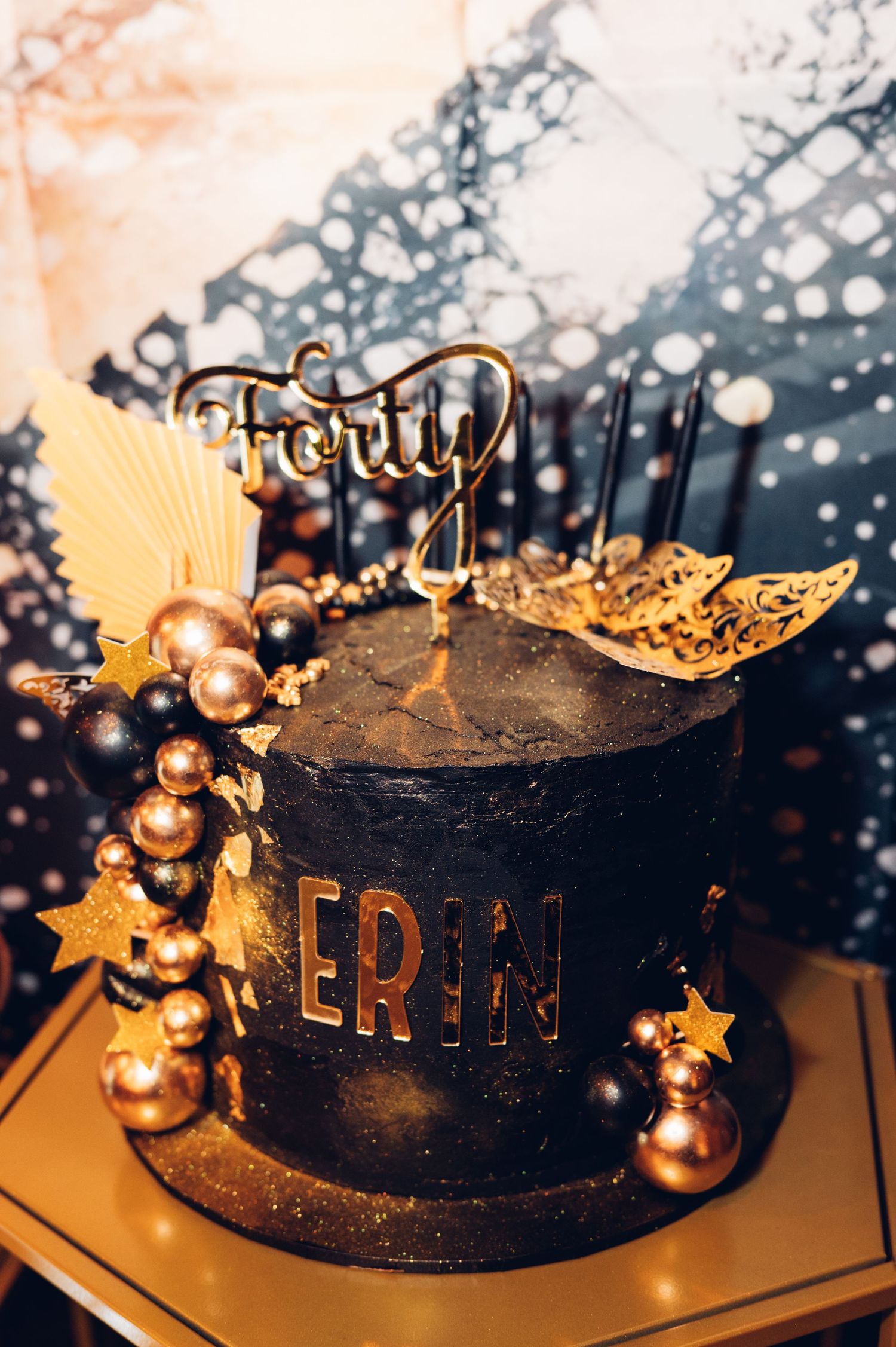 Black birthday cake decorated with gold ornaments and stars.