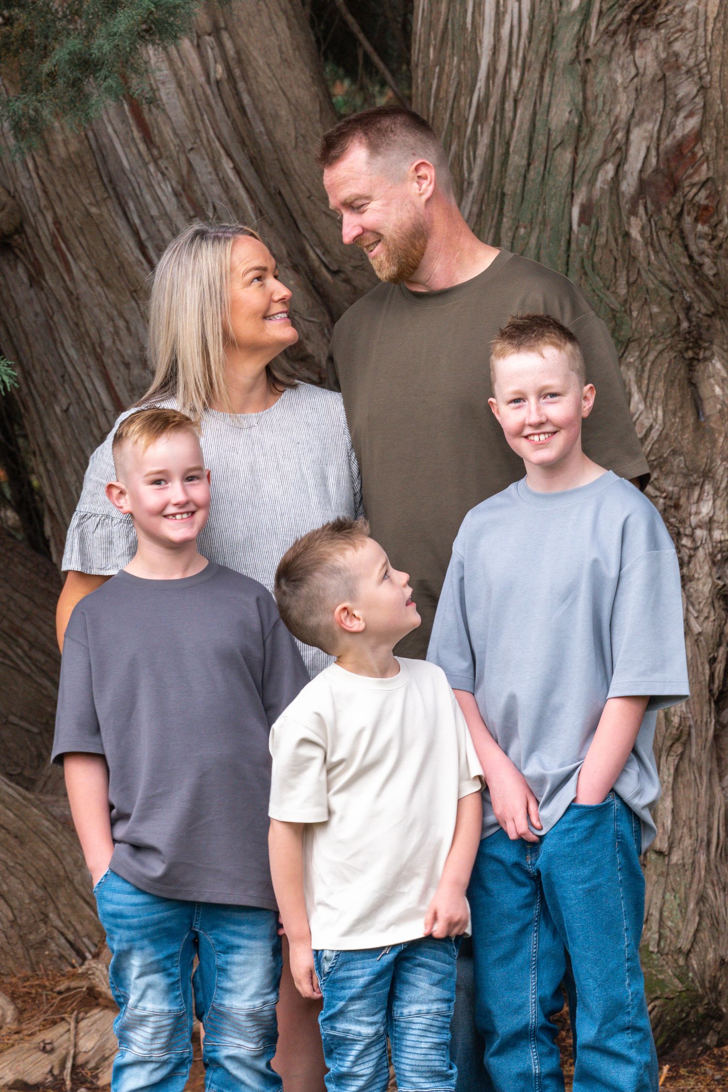 Candid family moment captured against rustic wooden backdrop wearing casual denim and t-shirts.