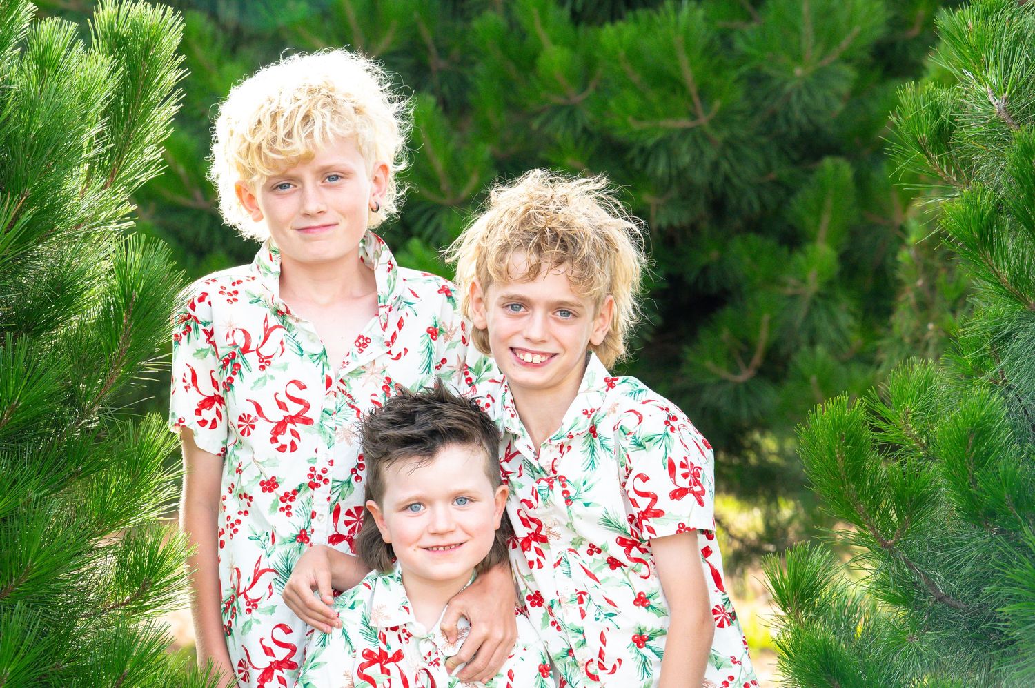 Outdoor family photo session among evergreen trees with coordinated white and red floral attire.