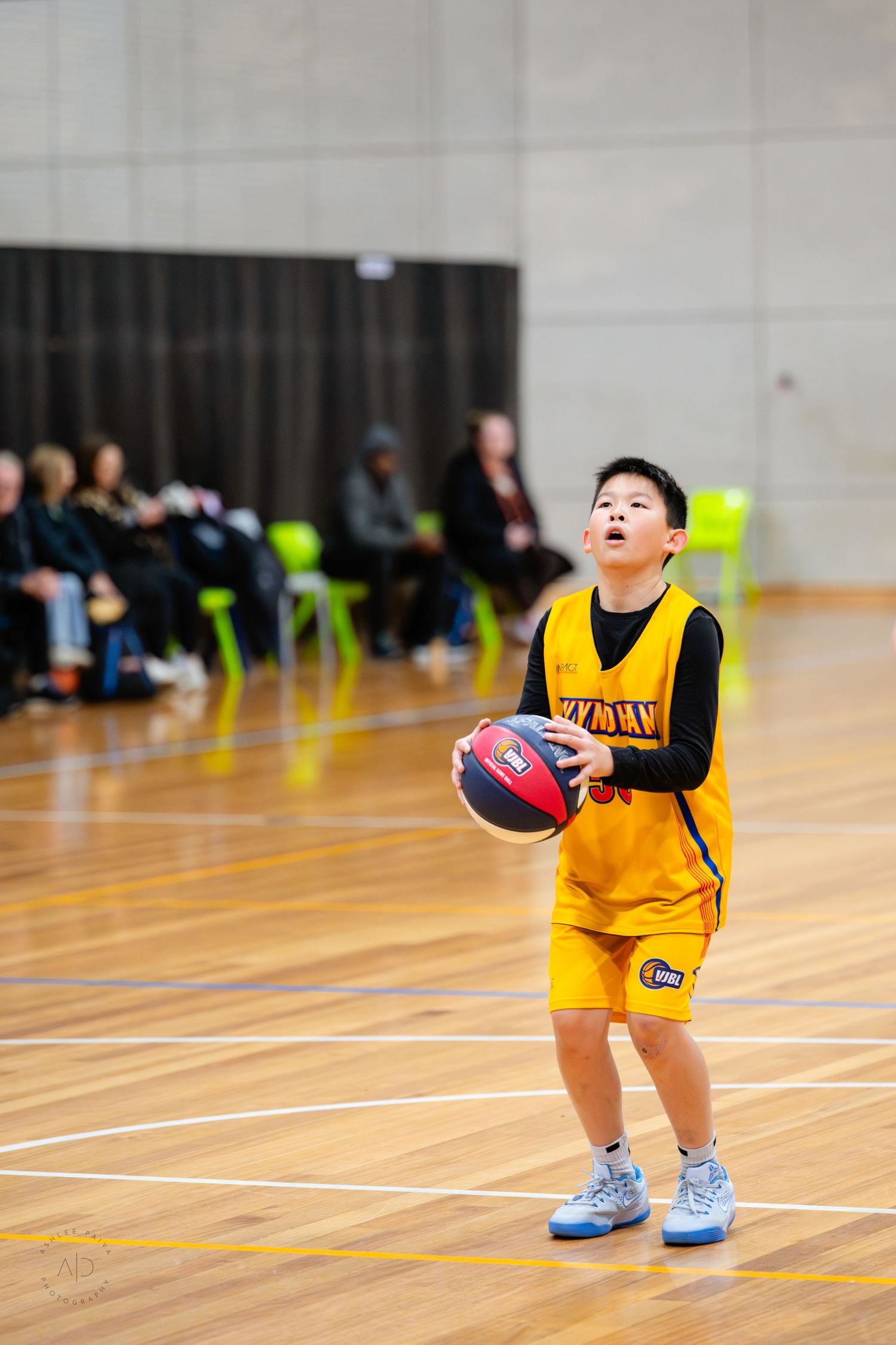 Young basketball player in yellow uniform prepares to shoot during an indoor junior basketball game.