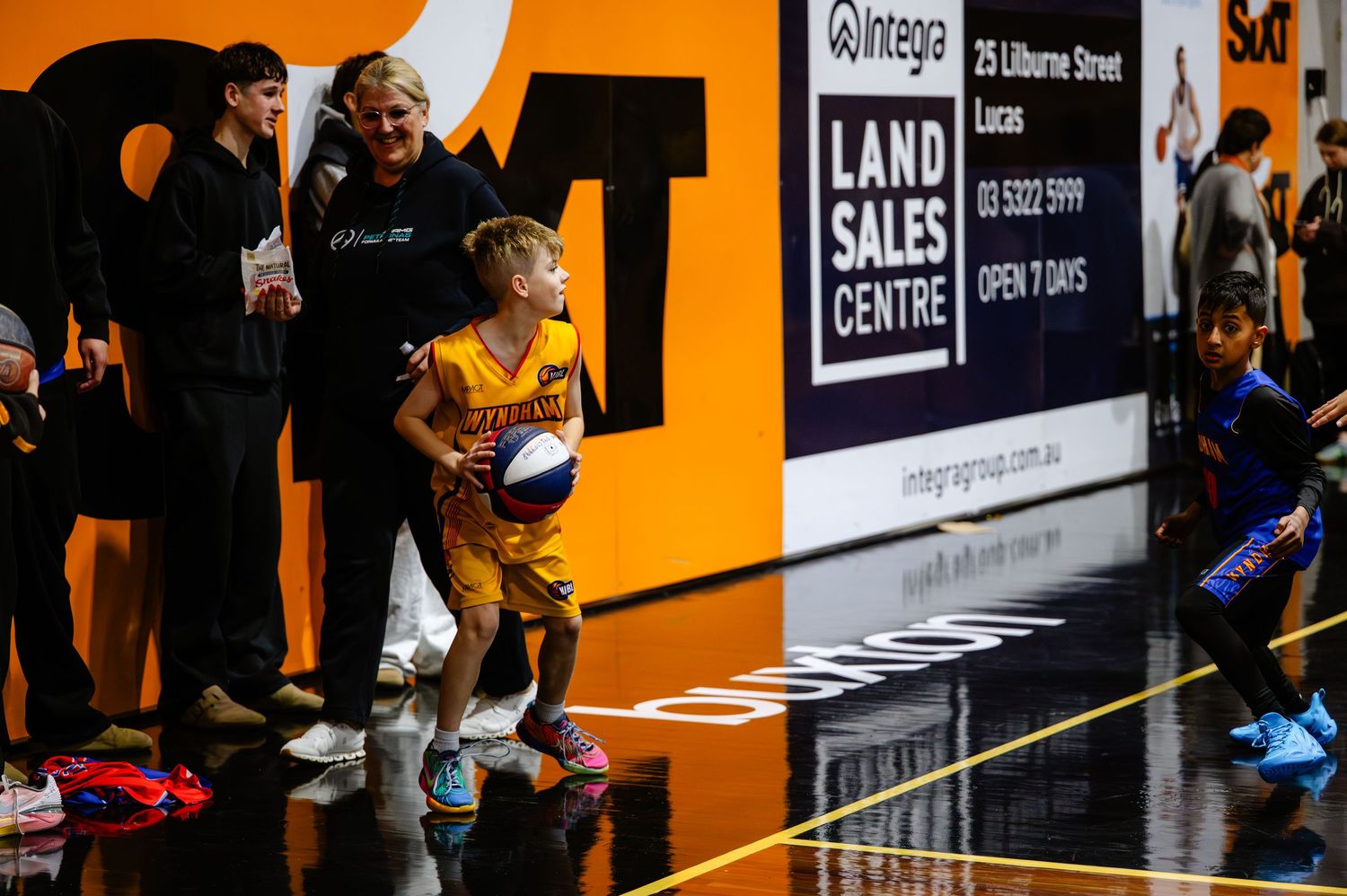 Young boy dribbling a basketball on an indoor court at a Land Sales Centre promotional event.