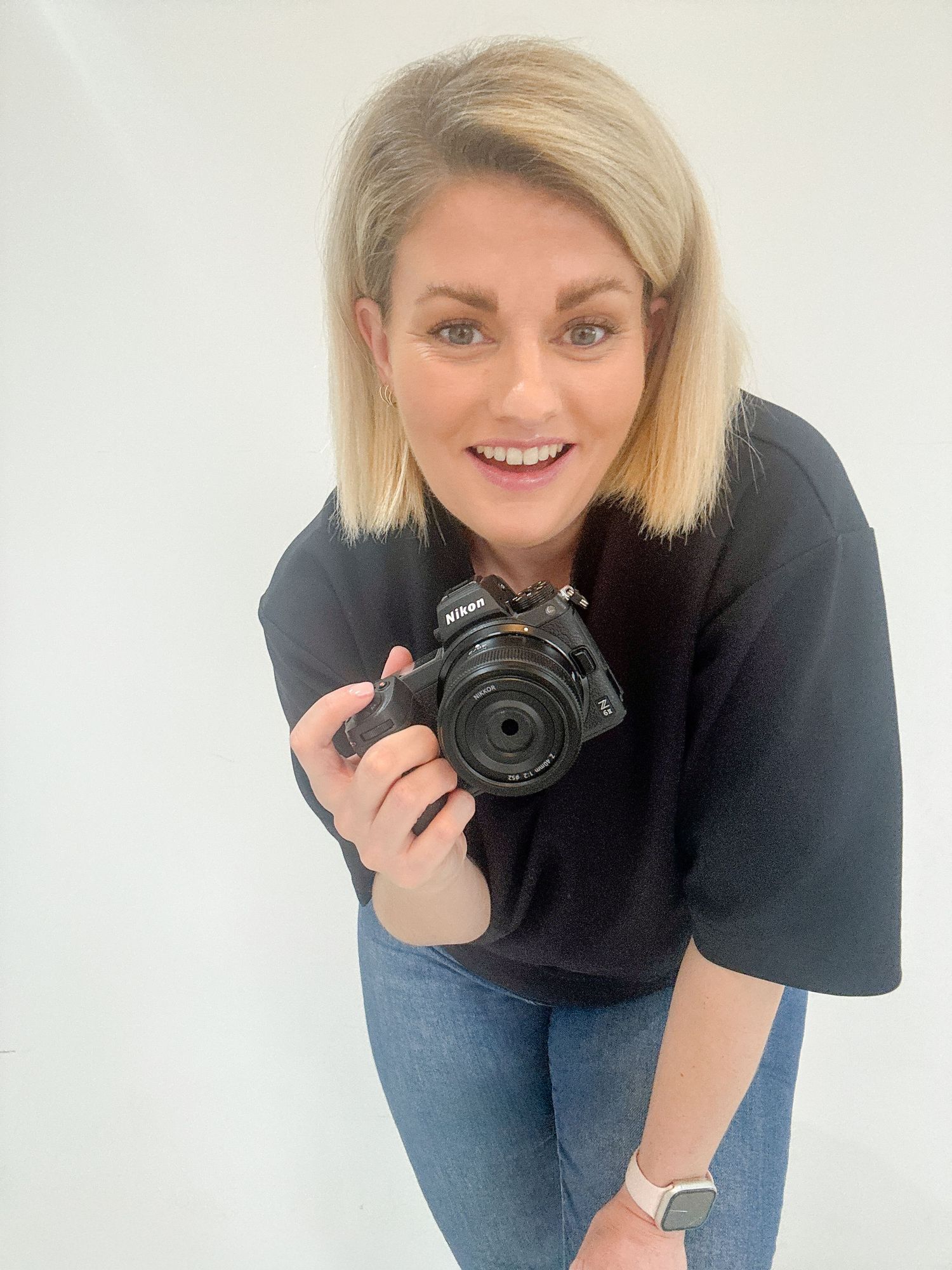 Playful photographer taking selfie with professional camera in studio setting.