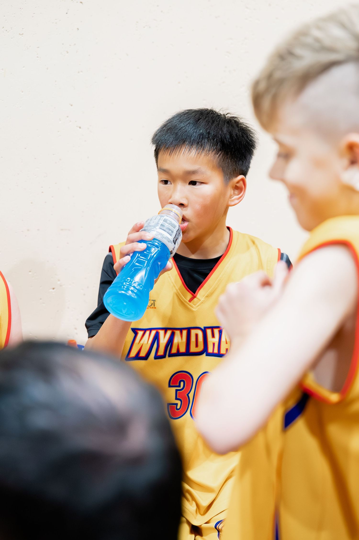 Young basketball player in Wyndham jersey #30 drinking blue sports drink during game break.