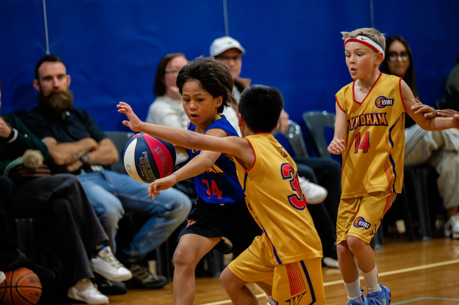 Young kids playing competitive basketball in a gymnasium, with players in yellow and blue uniforms dribbling and defending.